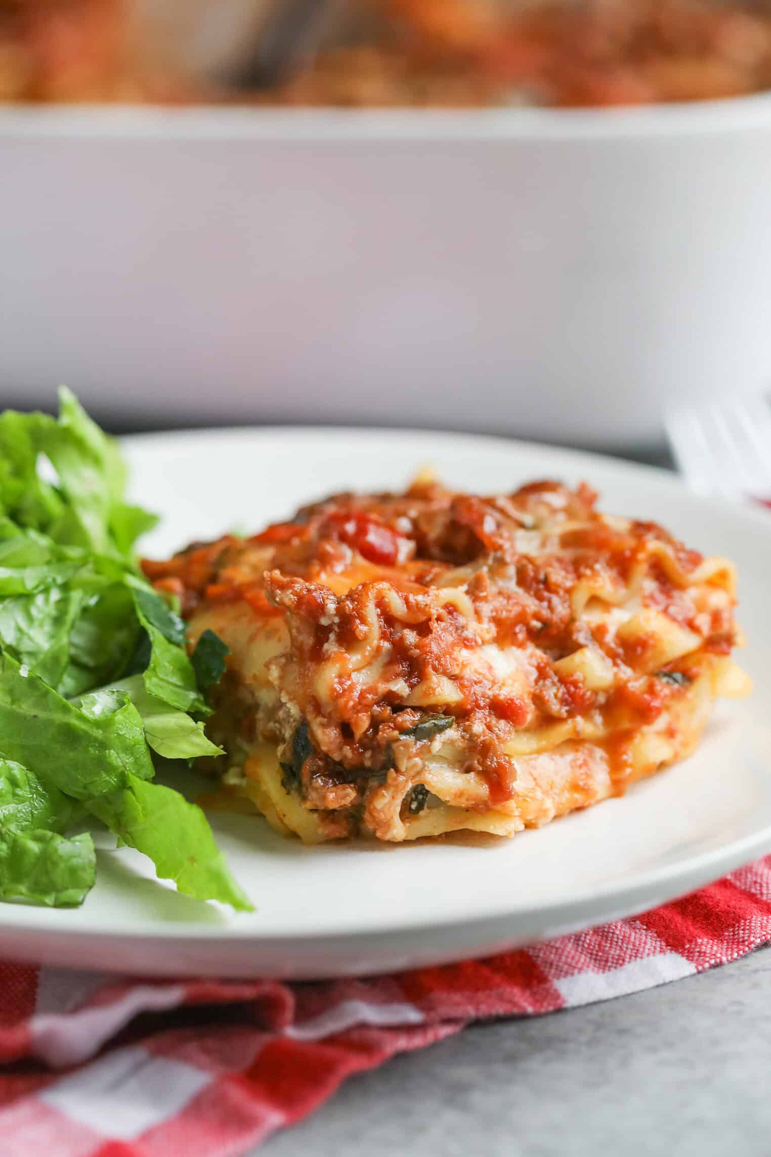 Impossible Lasagna 16 A Serving Of Impossible Lasagna Topped With Melted Cheese And Tomato Sauce Sits On A White Plate Next To A Small Side Of Fresh Green Lettuce. The Plate Rests On A Red And White Checkered Cloth.