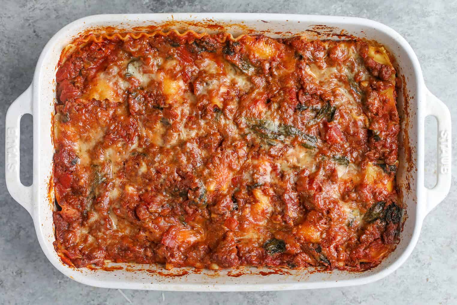 Impossible Lasagna 14 A Baked Impossible Lasagna In A White Rectangular Dish, Showing Layers Of Melted Cheese, Tomato Sauce, And Browned Edges. The Surface Appears Golden And Slightly Crispy With Visible Herbs And Sauce.