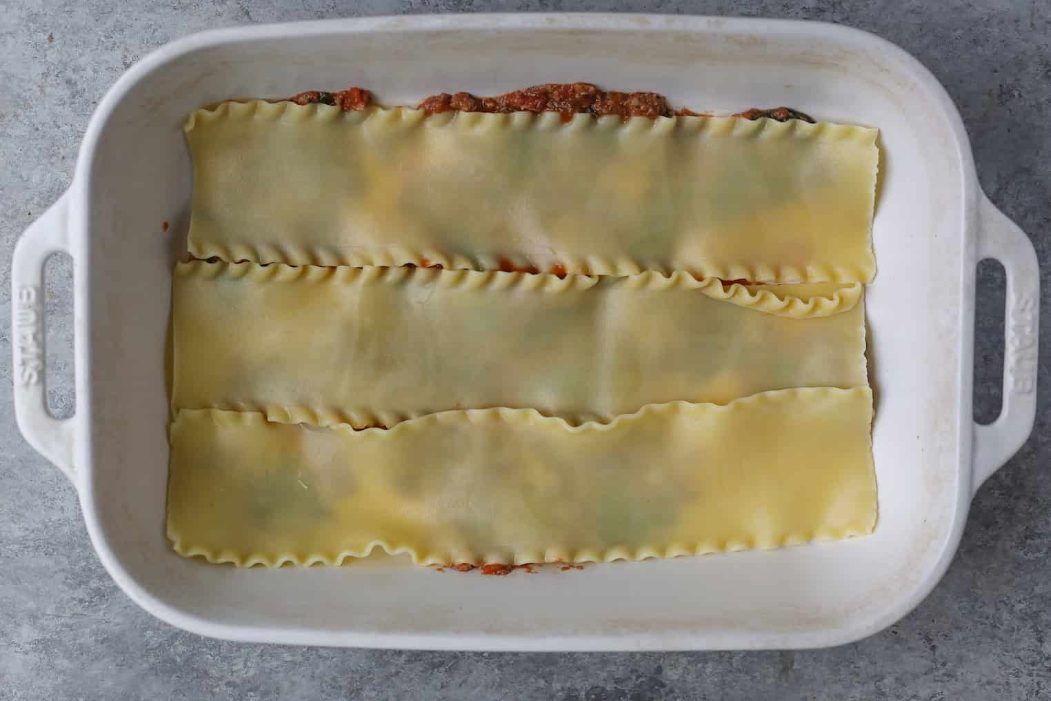 Impossible Lasagna 11 A White Baking Dish With A Layer Of Cooked Noodles Atop Tomato Sauce And Filling, This Impossible Lasagna Is Ready For The Next Step In Its Delicious Preparation.