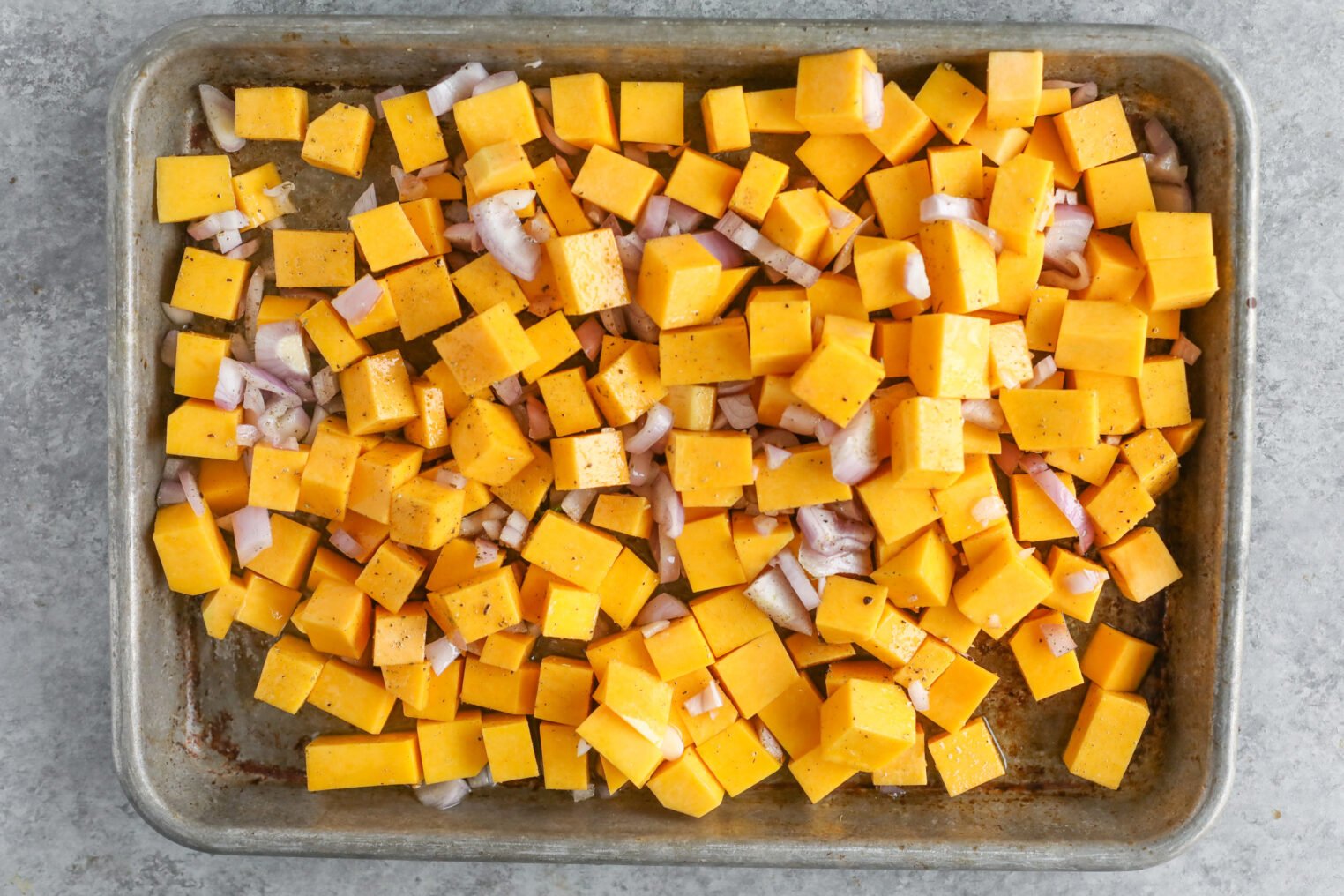 A Baking Sheet Filled With Evenly Spread Cubes Of Butternut Squash And Chopped Onions, Seasoned And Ready To Be Cooked For A Delicious Jeweled Farro Salad.