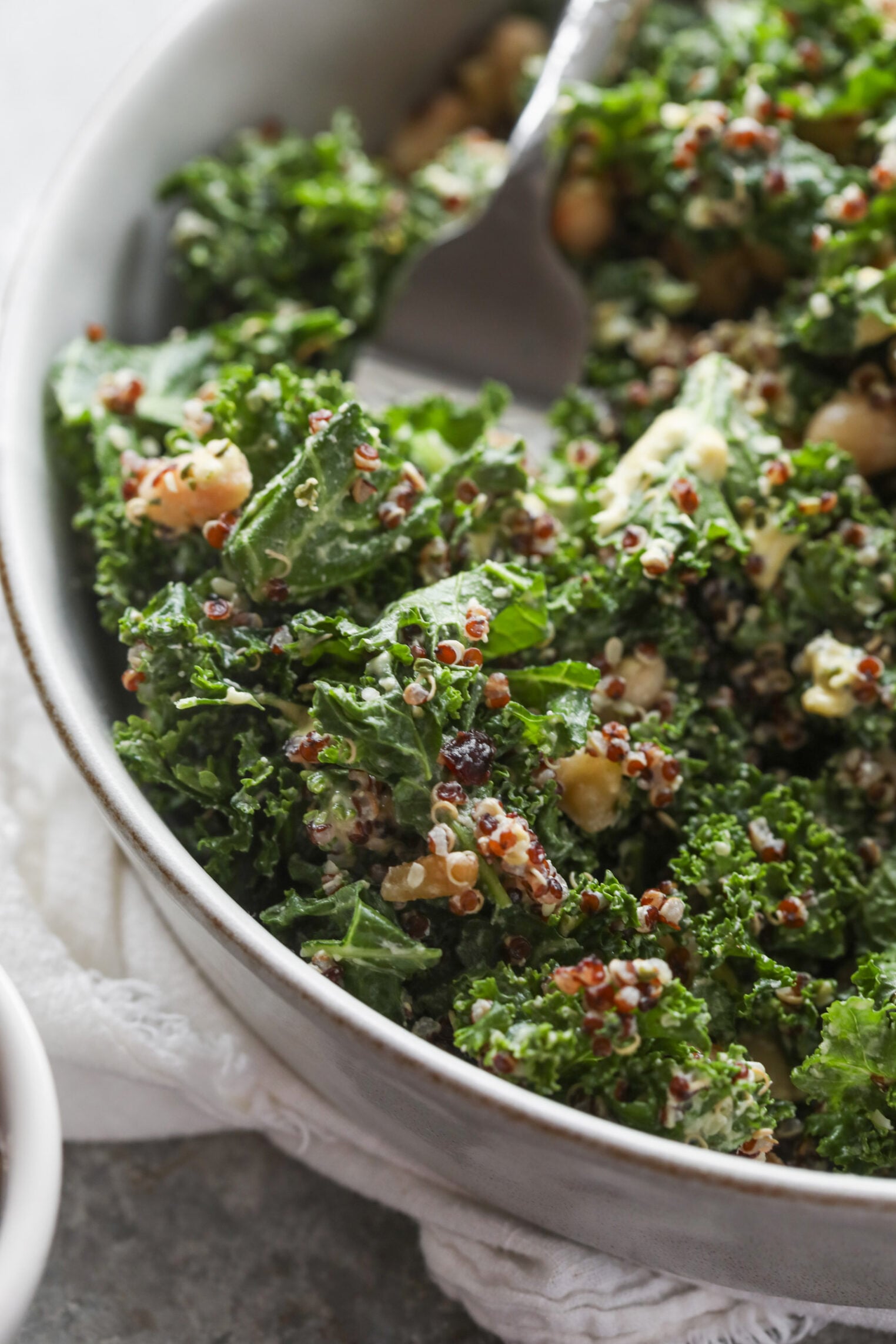 Quinoa Kale Salad 8 A Close-Up Of A Quinoa Kale Salad With Fresh Chickpeas And Creamy Dressing In A White Bowl, With A Fork Resting Inside.