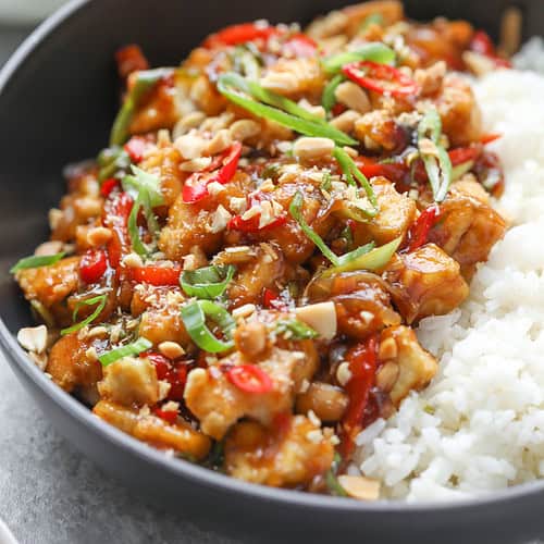 Kung Pao Tofu 14 A Bowl Of White Rice Topped With Kung Pao Tofu, Chopped Peanuts, Sliced Red And Green Chilies, And Green Onions, All Garnished With A Savory Sauce.