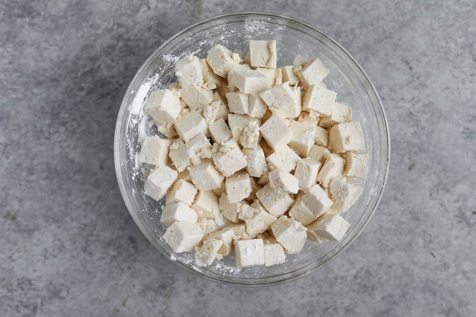 Kung Pao Tofu 6 A Glass Bowl Filled With Evenly Cut Cubes Of Tofu, Ready To Be Transformed Into A Flavorful Kung Pao Tofu Dish, Sits On A Gray Textured Surface.
