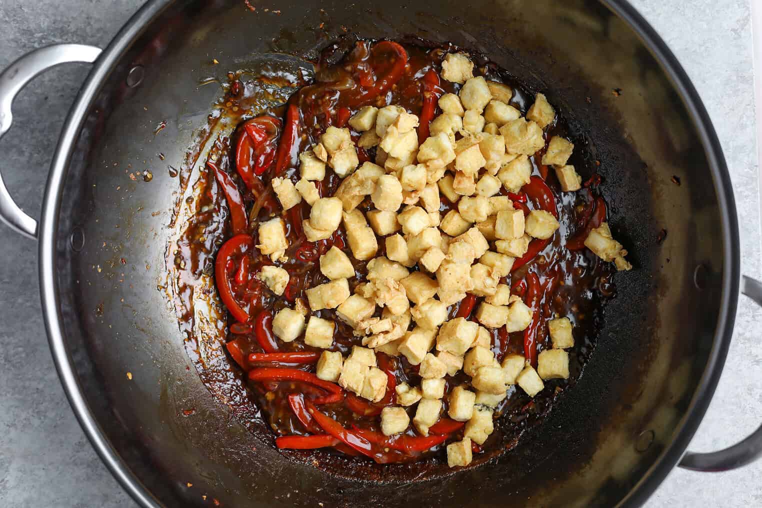 Kung Pao Tofu 9 A Wok Containing Kung Pao Tofu Features Stir-Fried Red Bell Peppers In A Savory Brown Sauce, Topped With Small Golden Cubes Of Fried Tofu.
