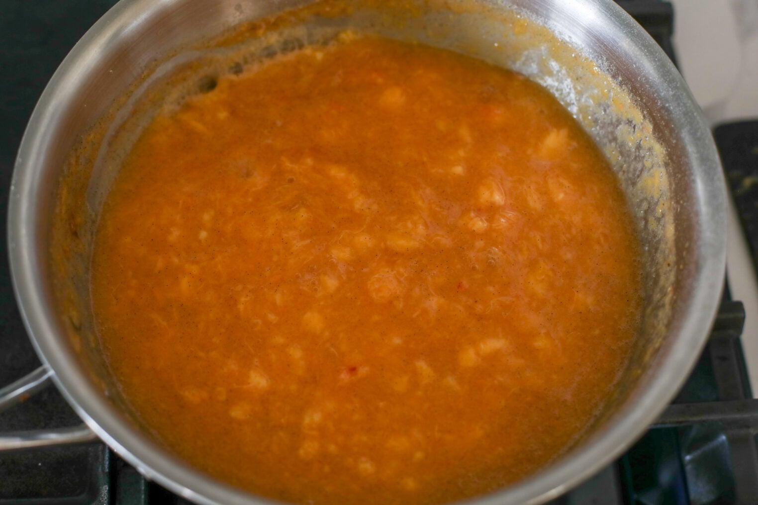 A Stainless Steel Pan On A Stove Contains A Thick, Orange-Brown Bubbling Sauce Or Stew With Visible Chunks, Reminiscent Of Homemade Low Sugar Peach Jam Simmering Gently.