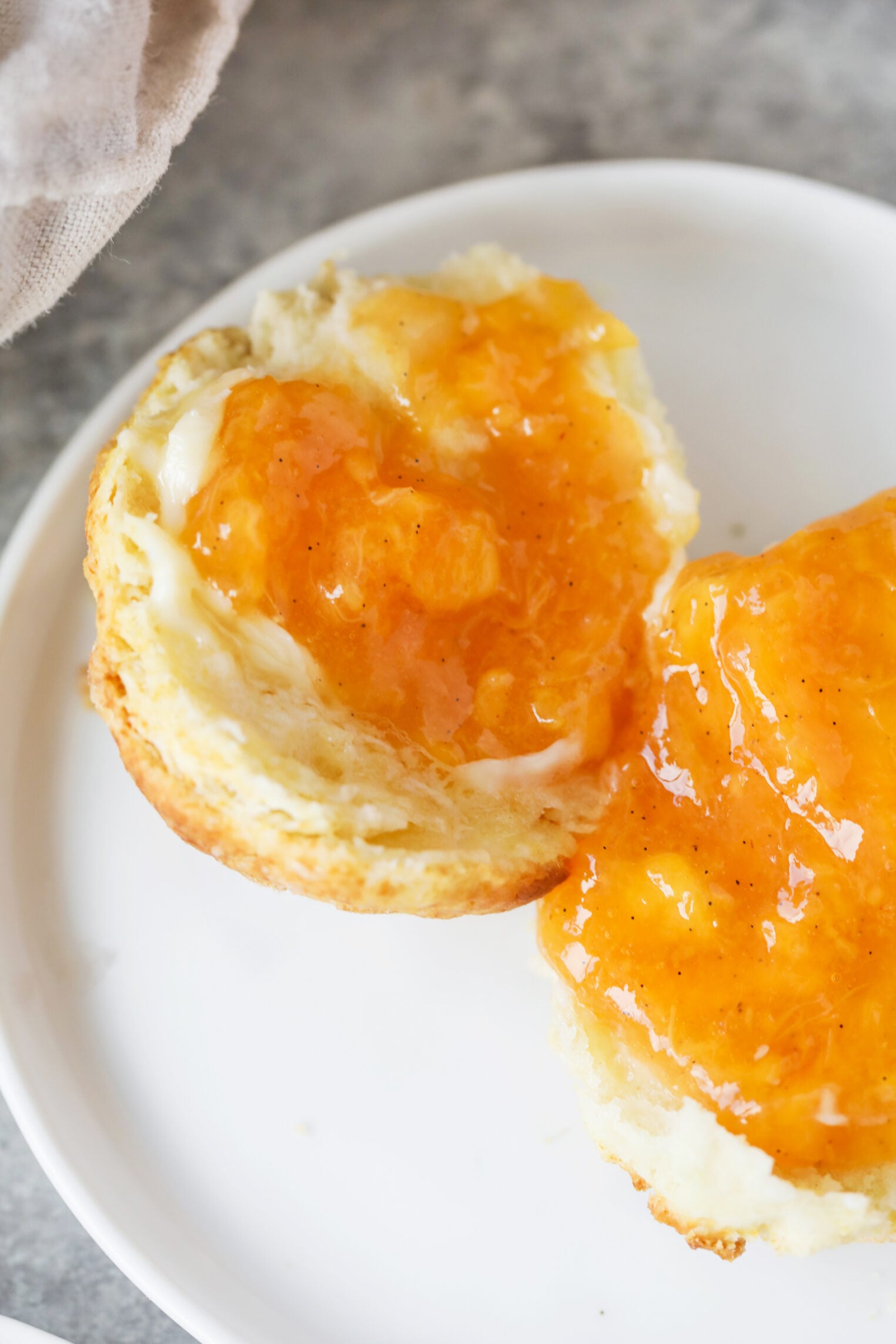 A Biscuit Split Open On A White Plate, Topped With A Generous Layer Of Golden Orange Low Sugar Peach Jam.