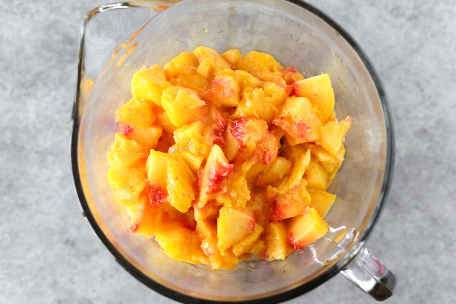 Chopped Yellow Peaches With Red Accents In A Glass Measuring Cup, Viewed From Above On A Gray Surface—Perfect For Making Low Sugar Peach Jam.