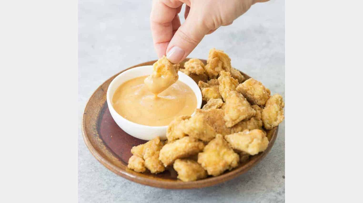 hand holding a tofu nugget with dipping sauce