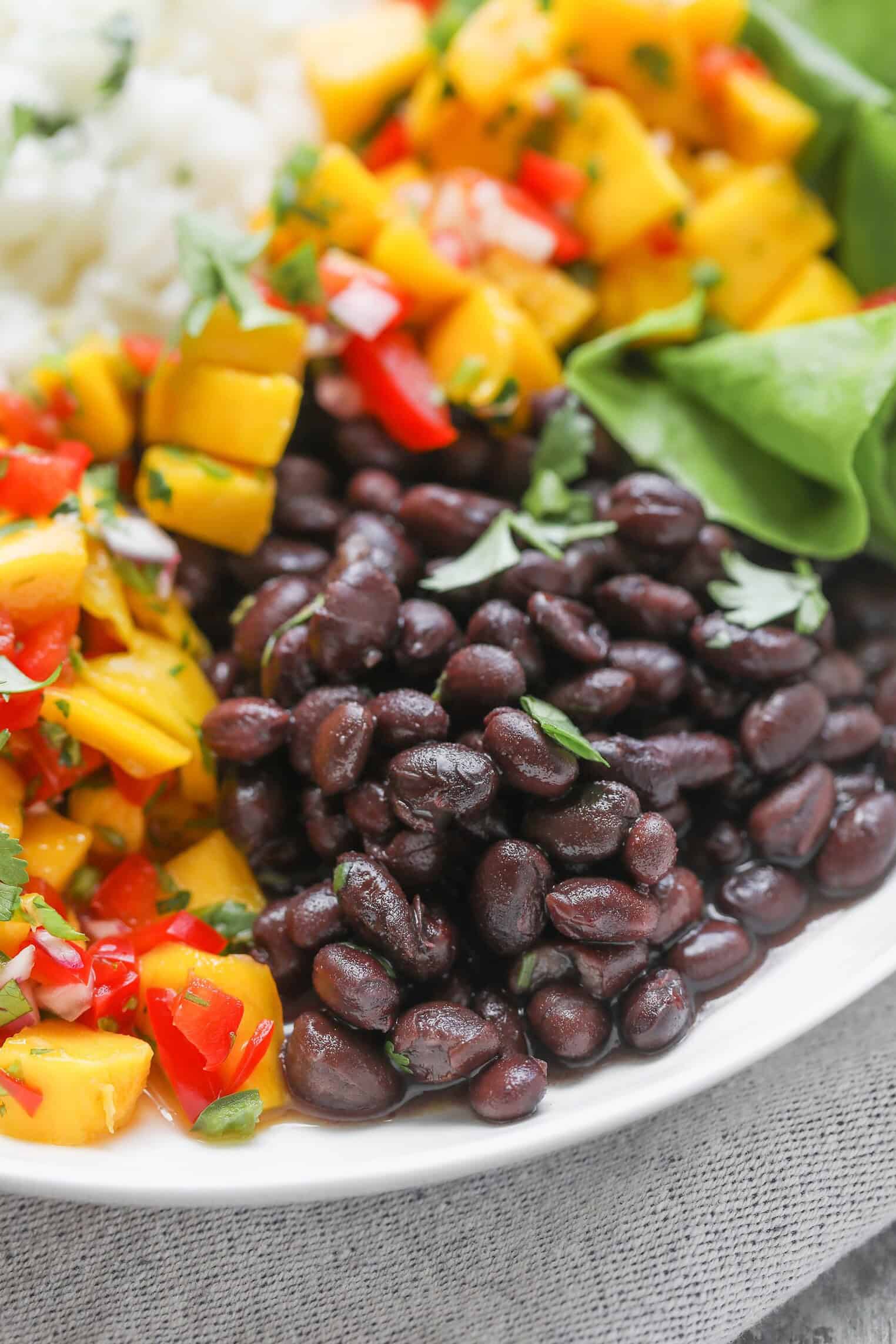 A Close-Up Of Vibrant Mango Salsa Bowls Featuring Black Beans, Diced Mango Salsa With Red Bell Peppers And Herbs, White Rice, And Fresh Green Lettuce Leaves. The Food Looks Colorful And Inviting.