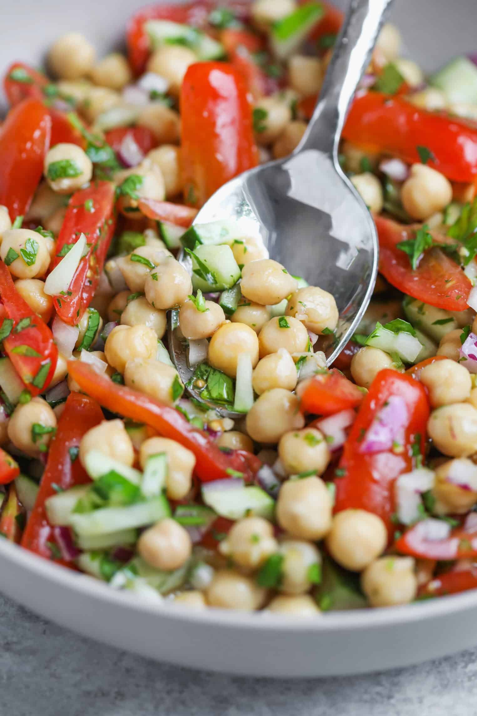 Marinated Chickpea Salad 3 A Close-Up Of A Vibrant Chickpea Salad With Sliced Tomatoes, Chopped Cucumber, Red Onion, And Fresh Herbs, With A Spoon Resting In The Bowl.