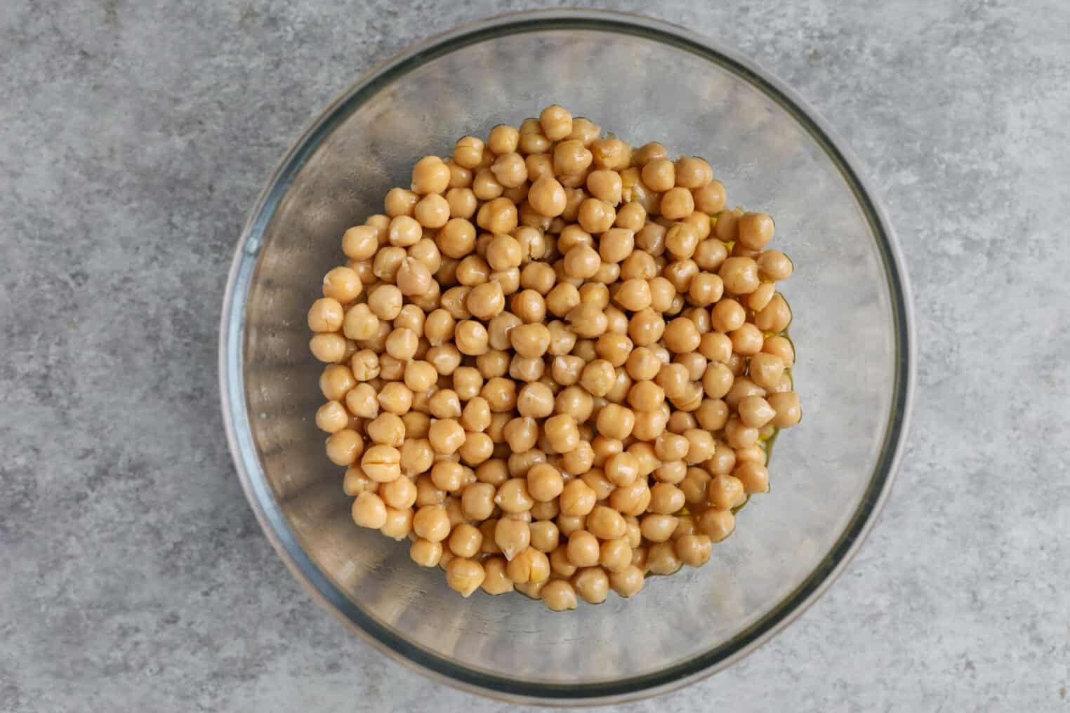 Marinated Chickpea Salad 4 A Glass Bowl Filled With Chickpea Salad Sits On A Gray, Textured Surface, Viewed From Above.