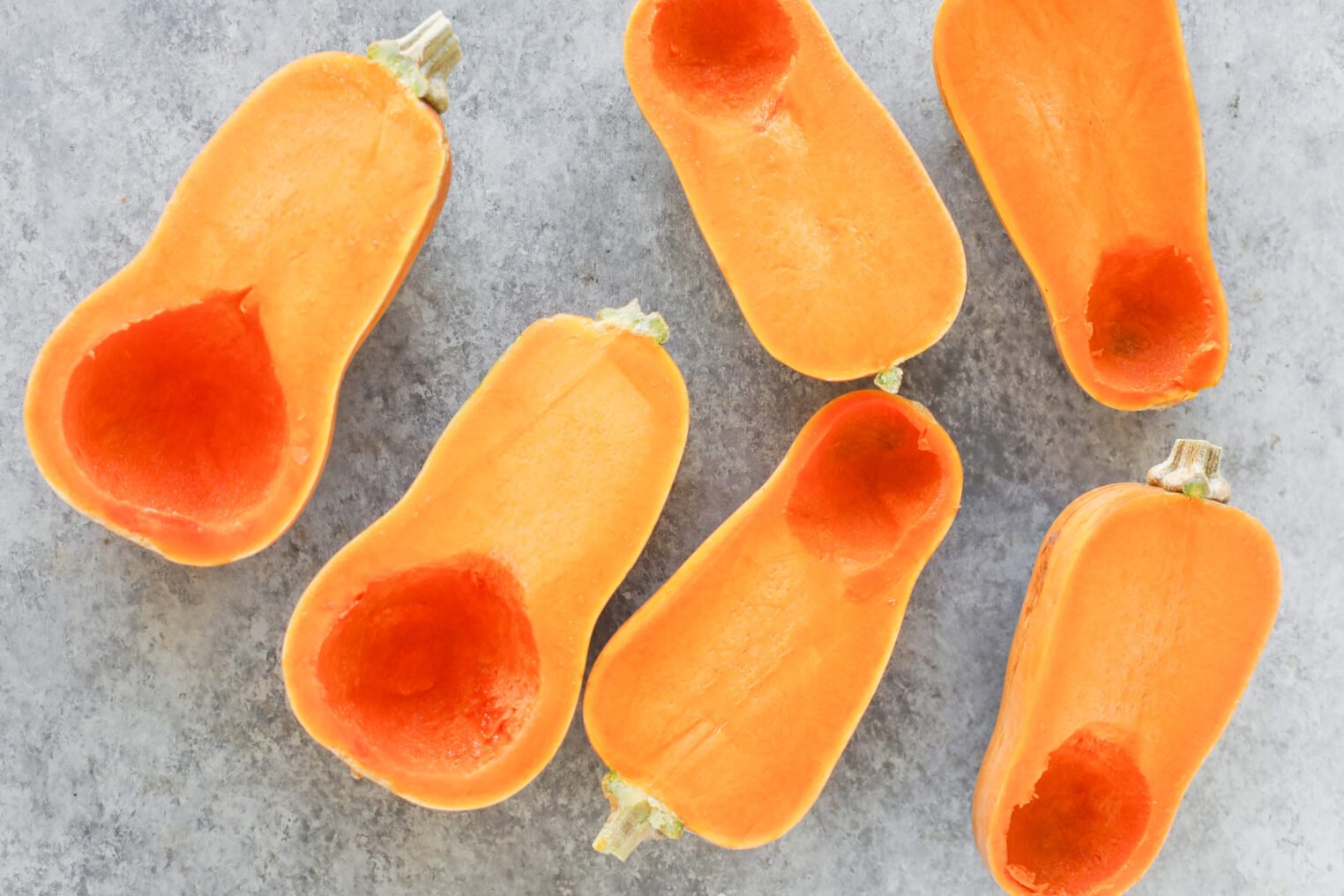 Miso Roasted Honeynut Squash 4 Six Roasted Honeynut Squash Halves With Seeds Removed, Arranged On A Light Gray Surface. The Vibrant Orange Flesh And Hollowed-Out Cavities Highlight The Rich Color And Inviting Texture Of The Squash.