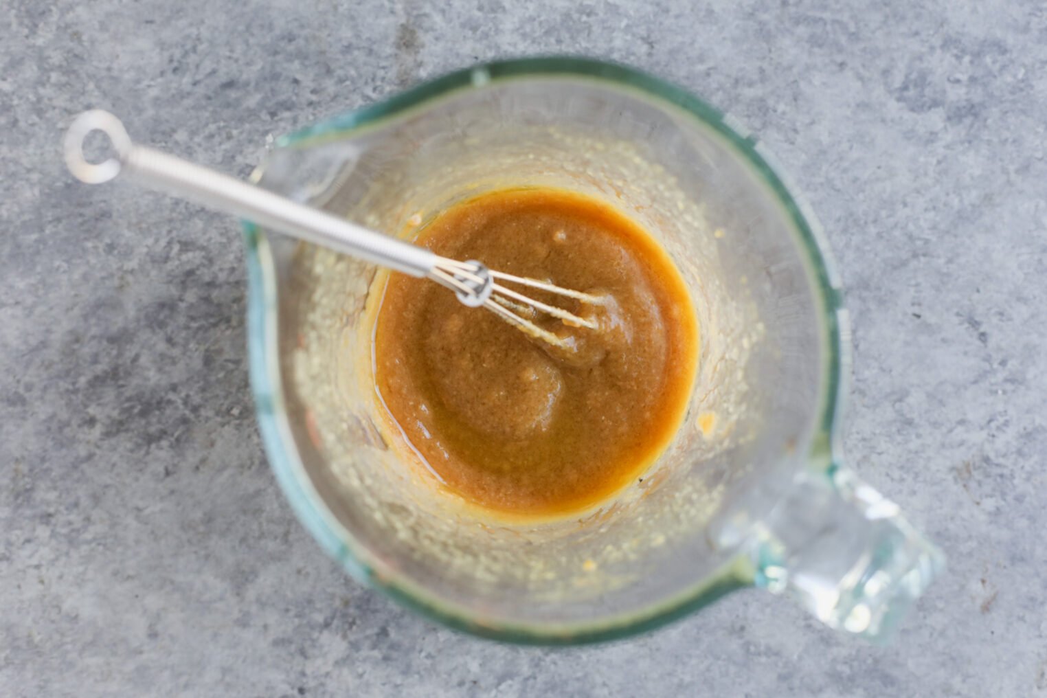 Miso Roasted Honeynut Squash 5 A Glass Measuring Cup With A Metal Whisk Inside Contains A Light Brown, Thick Roasted Honeynut Squash Mixture, Seen From Above On A Gray Textured Surface.