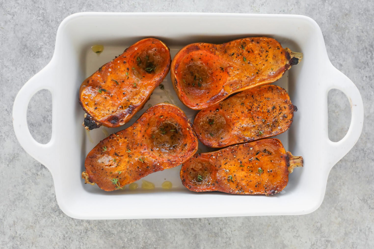 Miso Roasted Honeynut Squash 7 Five Roasted Honeynut Squash Halves, Perfectly Seasoned And Caramelized, Are Arranged In A White Rectangular Baking Dish On A Light Gray Surface.
