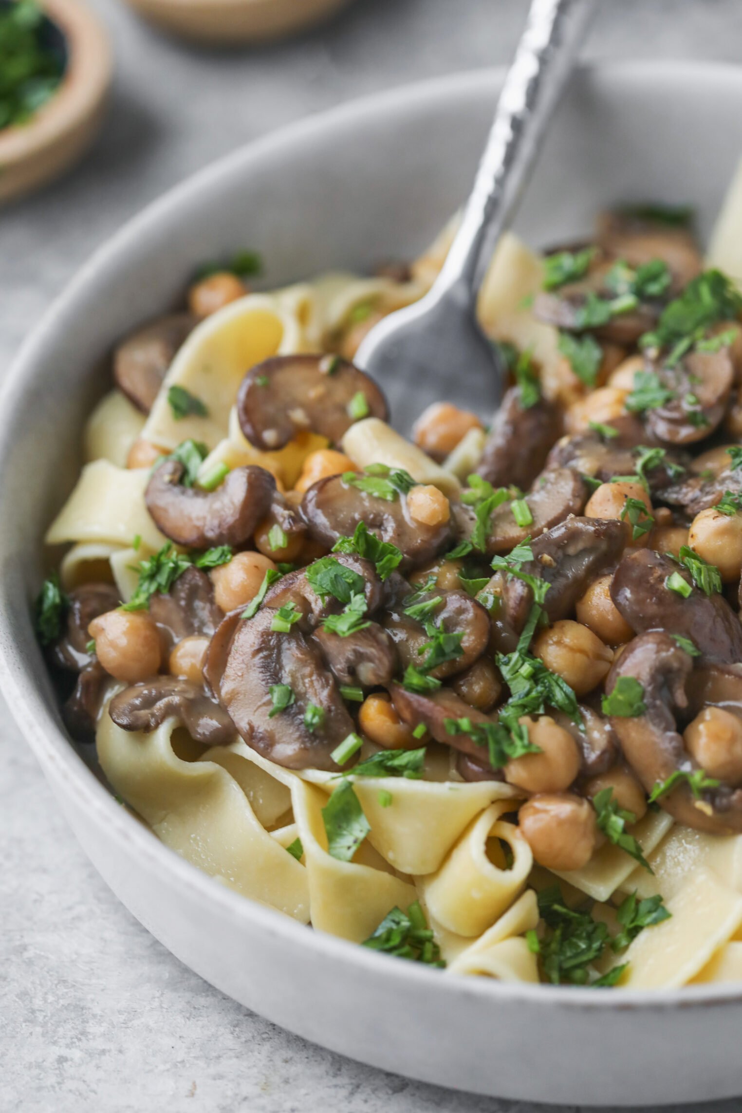 Mushroom Marsala with Chickpeas 1 A Close-Up Of A Bowl Of Wide Pasta Noodles Topped With Savory Mushroom Marsala, Chickpeas, And Fresh Chopped Herbs, With A Fork Resting In The Bowl.