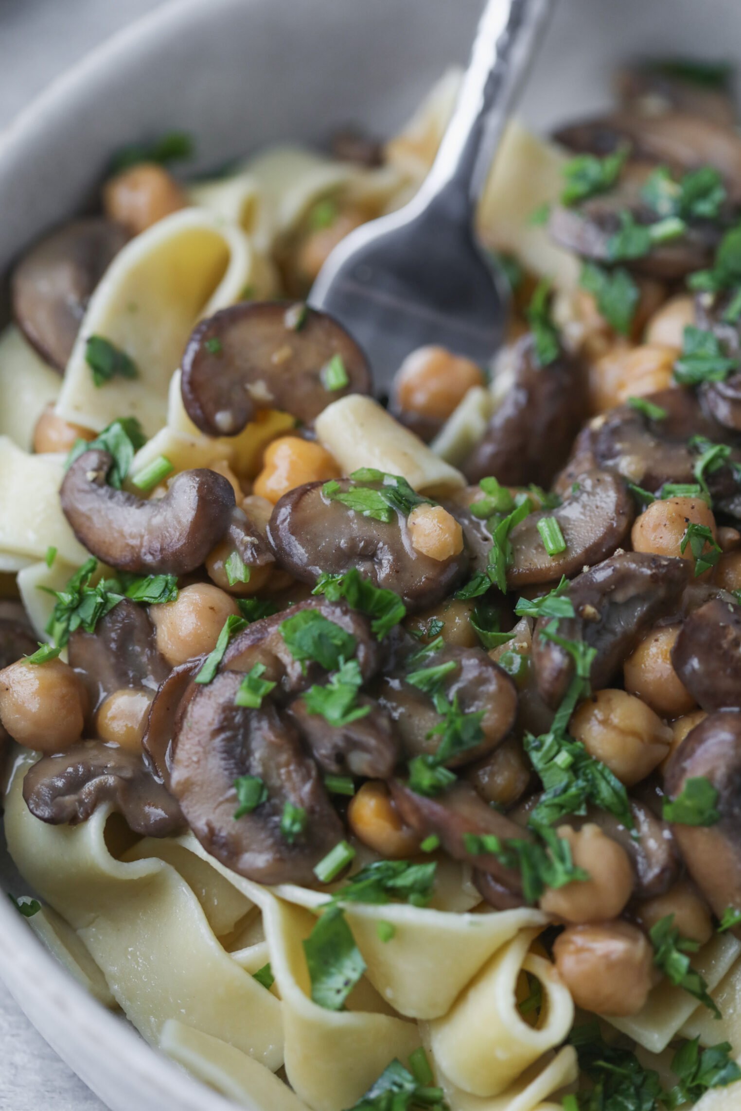 Mushroom Marsala with Chickpeas 8 A Close-Up Of A Bowl Of Pasta Topped With Sautéed Mushroom Marsala, Chickpeas, And Chopped Fresh Herbs, With A Fork Twirling Some Noodles.
