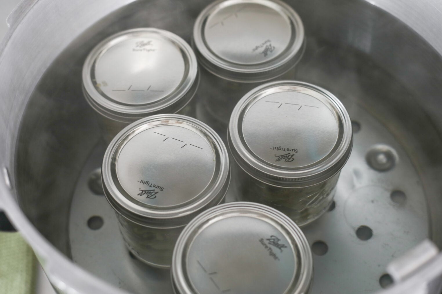 Pickled Jalapeños (Canning Recipe) 8 Four Closed Glass Jars, Possibly Filled With Pickled Jalapenos, Are Being Sterilized In A Steaming Metal Pot, Likely For Canning Or Preserving Food. The Jars Sit On A Rack Inside The Pot, And Condensation Is Visible On Their Surfaces.