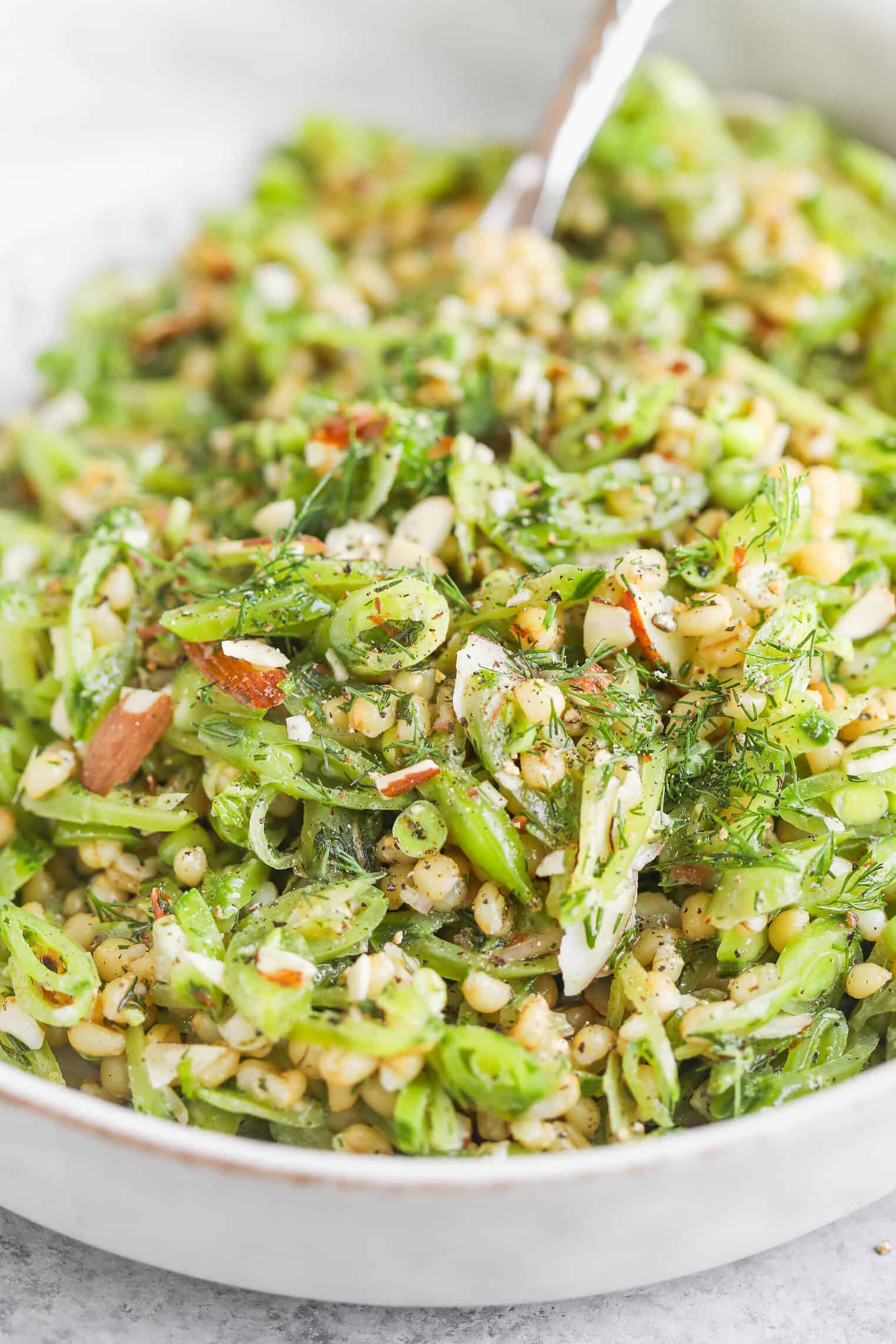 A Close-Up Of A Fresh Farro Salad With Sliced Green Beans, Spring Peas, Chopped Almonds, Mint, Herbs, And A Light Dressing, Served In A White Bowl With A Fork.