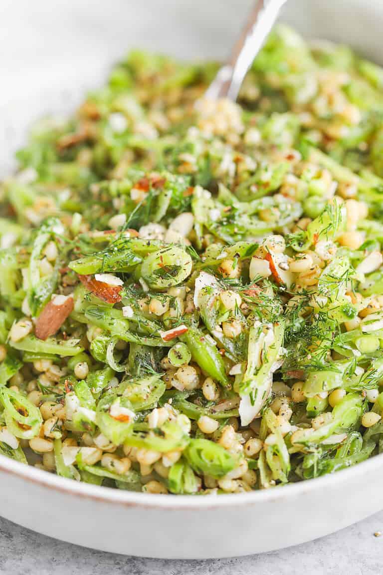 A Close-Up Of A Fresh Farro Salad With Sliced Green Beans, Spring Peas, Chopped Almonds, Mint, Herbs, And A Light Dressing, Served In A White Bowl With A Fork.
