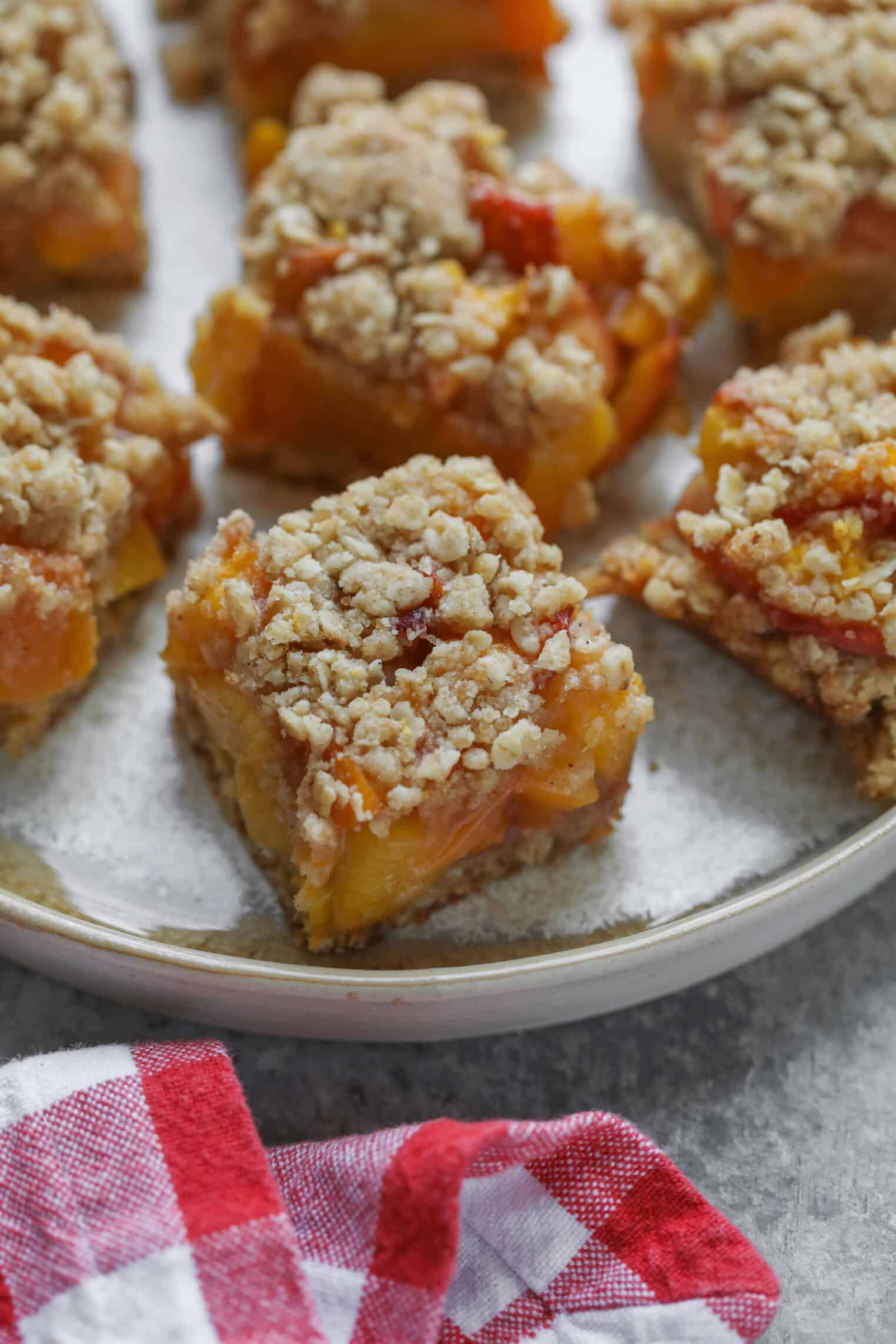 Peach Pie Bars 10 Several Squares Of Peach Pie Bars Are Arranged On A Round Plate. The Dessert Bars Have A Golden Crumbly Topping And A Visible Peach Filling. A Red And White Checkered Cloth Is Partially Visible In The Foreground.