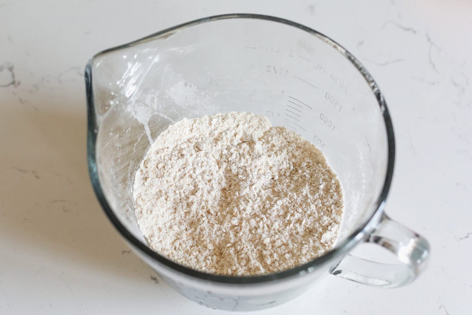 Peach Pie Bars 4 A Clear Glass Measuring Cup Filled With A Mixture Of Dry Oatmeal And Flour Sits On A White Countertop, Ready To Be Used In A Delicious Batch Of Peach Pie Bars.