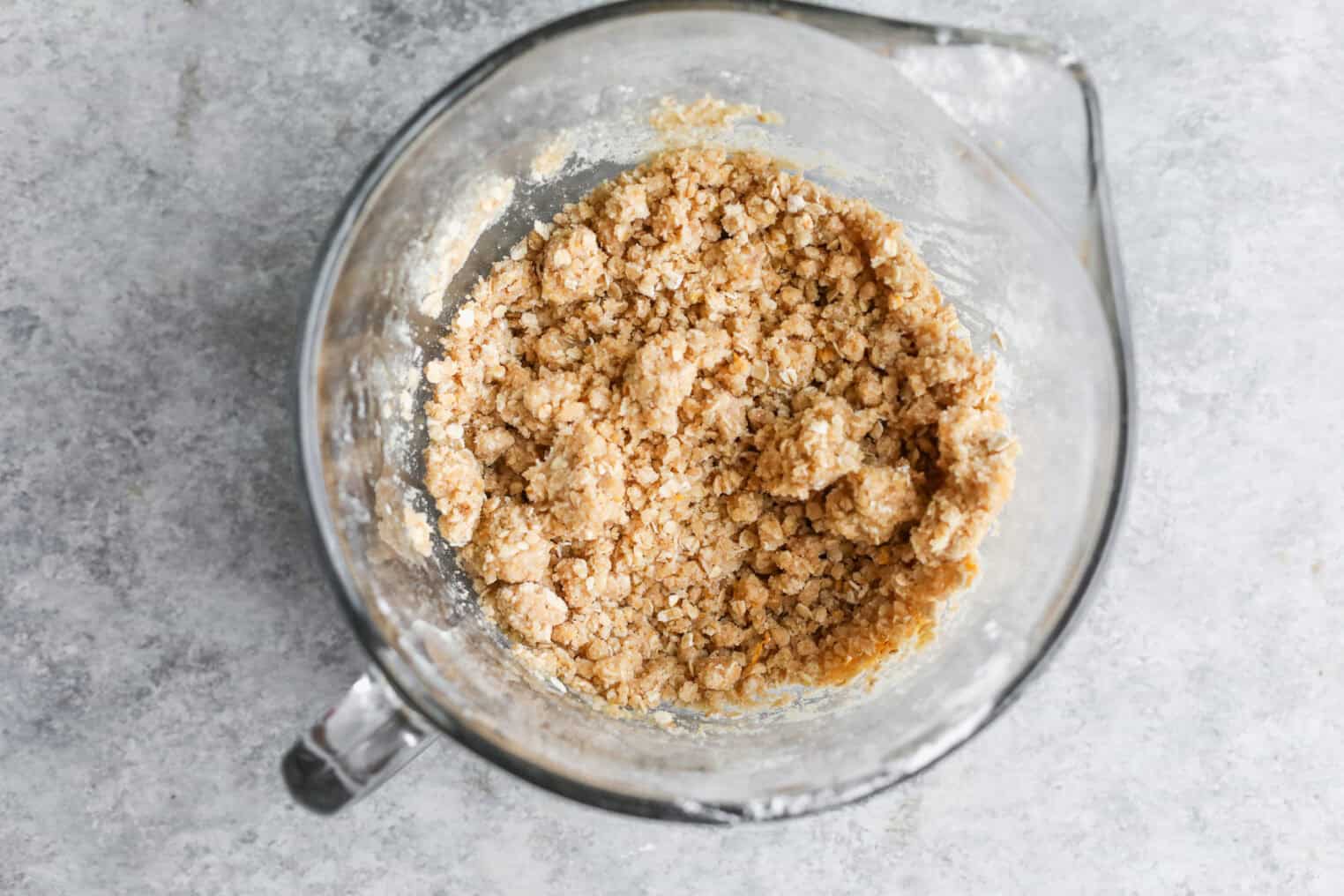 Peach Pie Bars 5 A Glass Mixing Bowl Filled With Crumbly Dough Mixture For Peach Pie Bars Sits On A Light Gray Countertop, Viewed From Above.