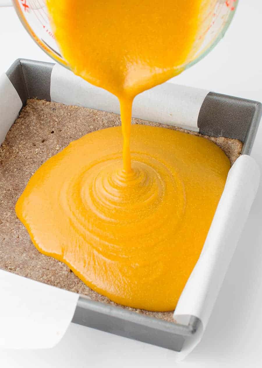 Pouring the pumpkin filling over the pecan pie base 