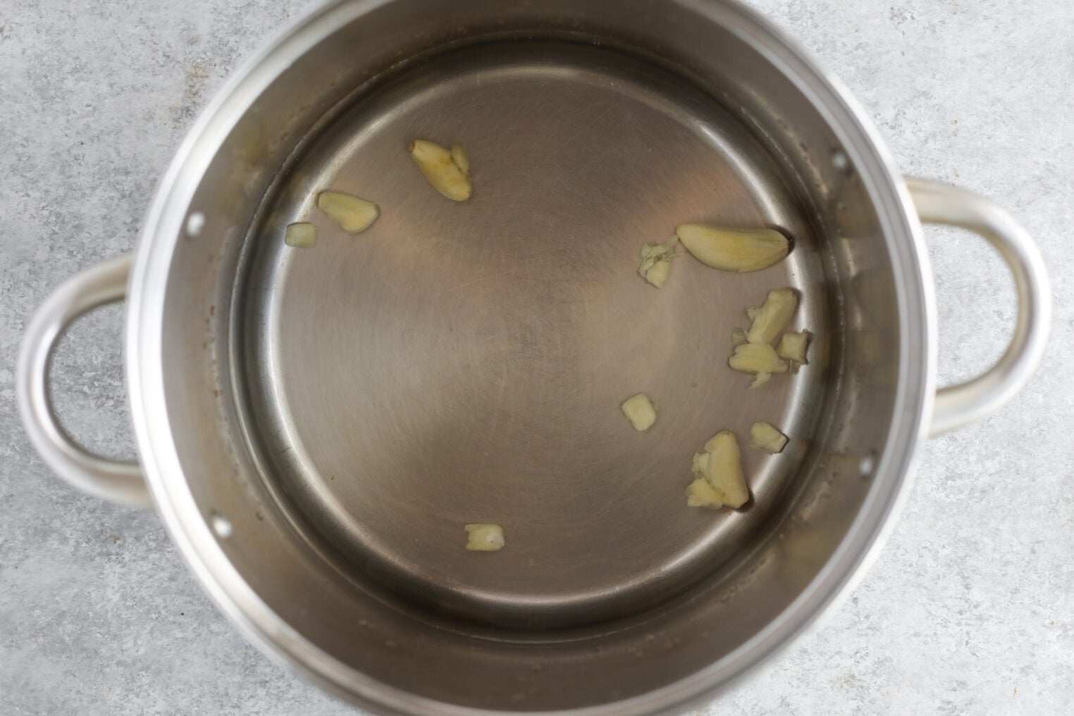 Pickled Jalapeños (Canning Recipe) 6 A Stainless Steel Pot With A Few Chopped Pieces Of Garlic And Some Pickled Jalapenos Inside, Resting On A Light Gray Countertop.