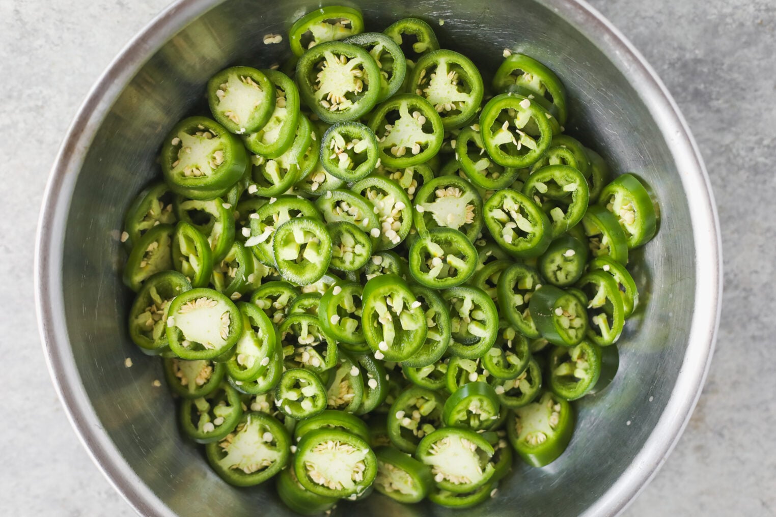 Pickled Jalapeños (Canning Recipe) 5 A Metal Bowl Filled With Sliced Fresh Green Jalapeño Peppers, Showing Seeds And White Pith—Perfect For Making Pickled Jalapenos—On A Light Gray Surface.