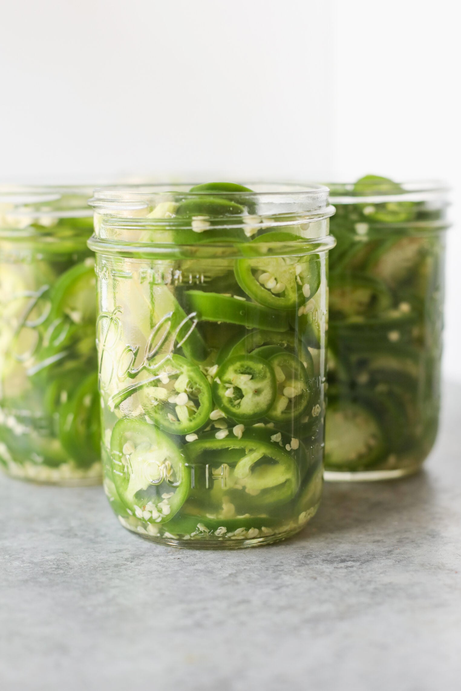 Pickled Jalapeños (Canning Recipe) 1 Three Glass Jars Filled With Sliced Green Jalapeños And Brine Are Placed On A Gray Surface With A White Background—Perfect For Showcasing Your Favorite Pickled Jalapeño Recipe Or Canning Recipe At Home.