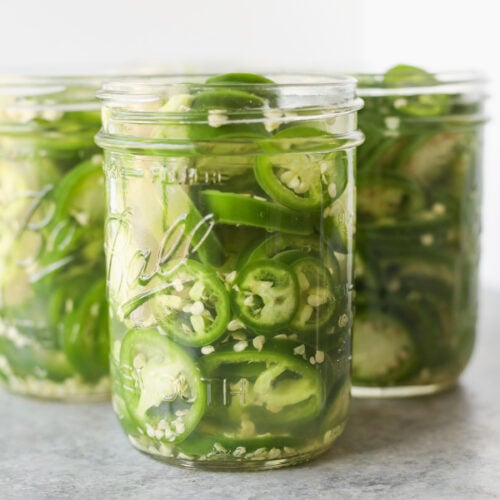 Pickled Jalapeños (Canning Recipe) 12 Three Glass Jars Filled With Sliced Green Jalapeños And Brine Are Placed On A Gray Surface With A White Background—Perfect For Showcasing Your Favorite Pickled Jalapeño Recipe Or Canning Recipe At Home.