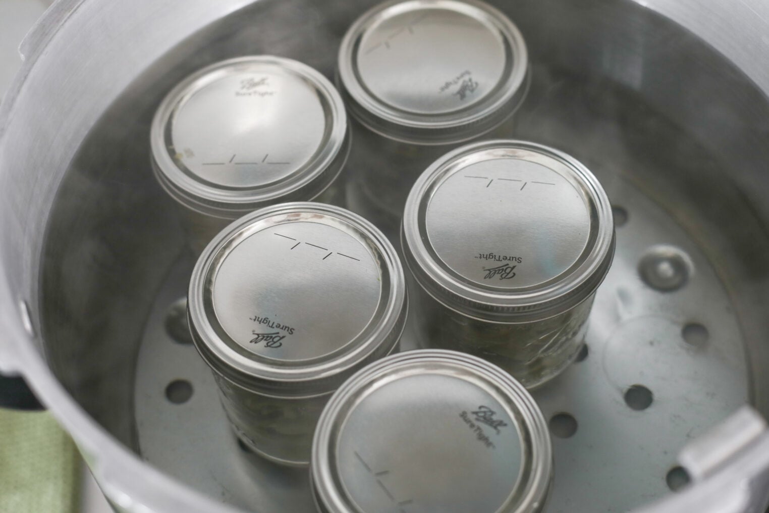 Four Sealed Glass Canning Jars With Metal Lids Are Being Processed In A Large Pot With Steam Rising, Likely For Preserving Food Such As Homemade Bread And Butter Pickles.