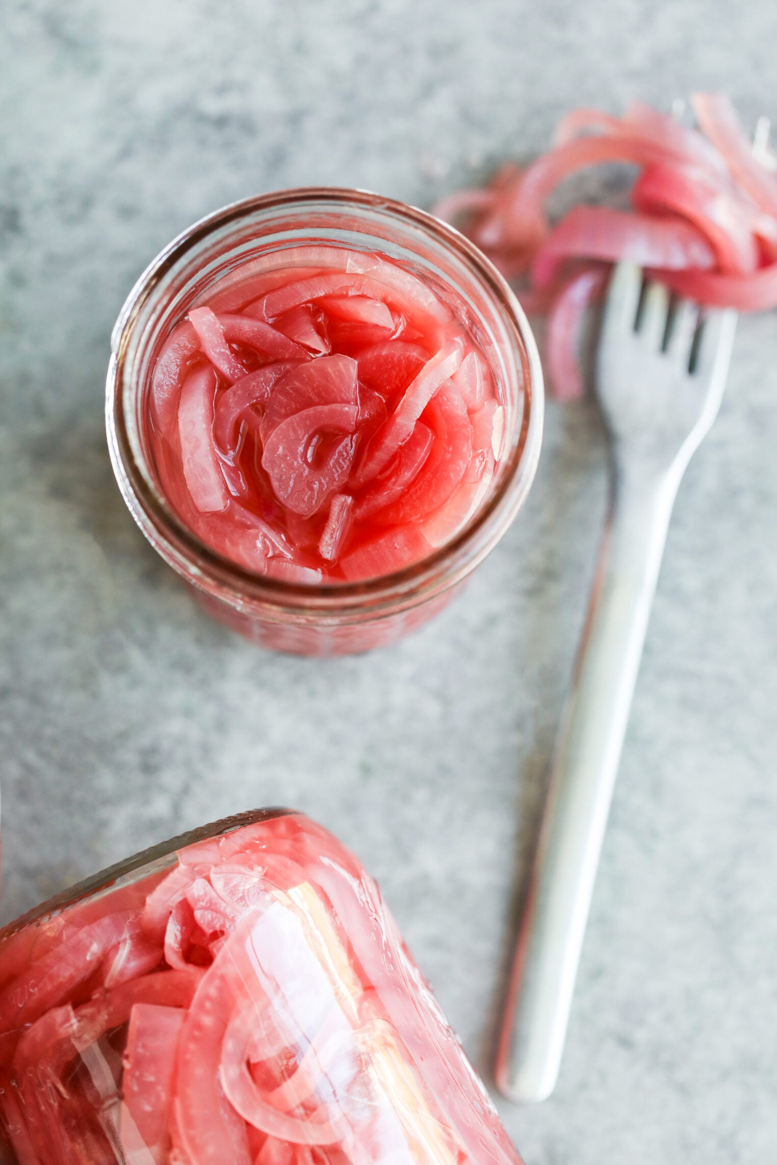 Pickled Red Onions 2 A Glass Jar Filled With Pickled Red Onions, With A Fork And Extra Onions Resting Beside It.
