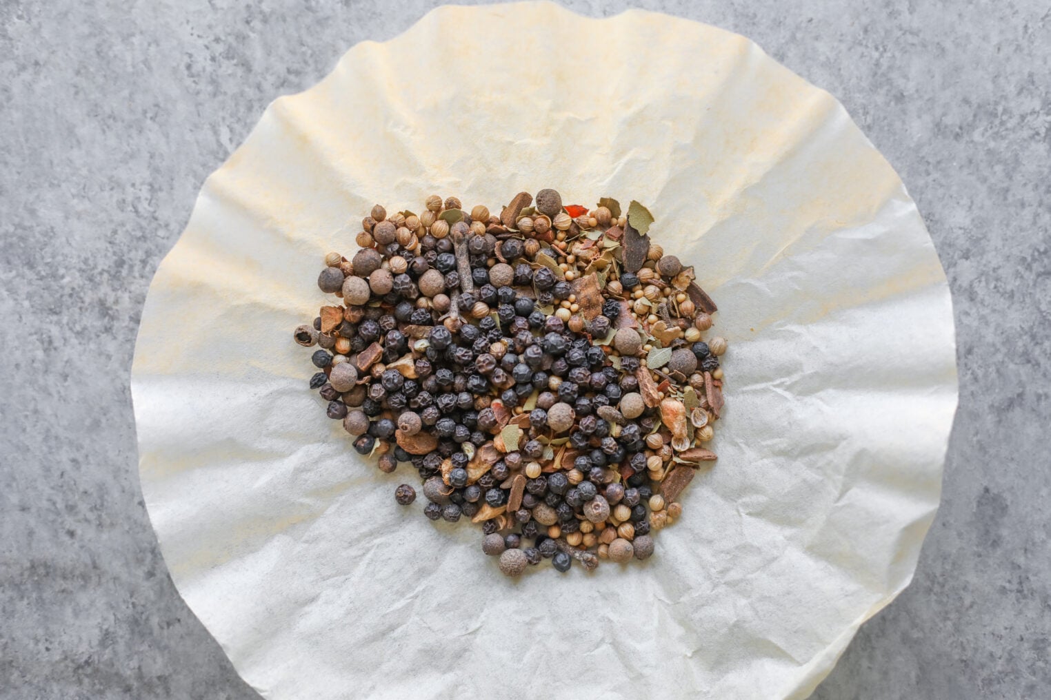 Pickled Red Onions 5 A Pile Of Mixed Whole Spices, Including Peppercorns And Coriander Seeds Used For Pickled Red Onions, Resting On A Round Paper Coffee Filter.