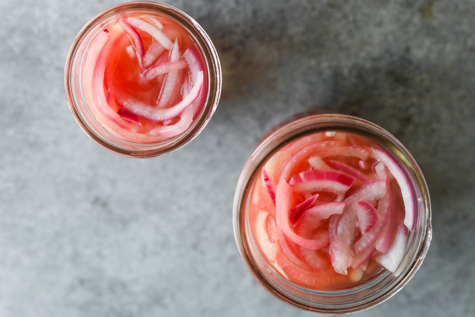Pickled Red Onions 7 A Top-Down View Of Two Glass Jars Filled With Pink Pickled Red Onions.