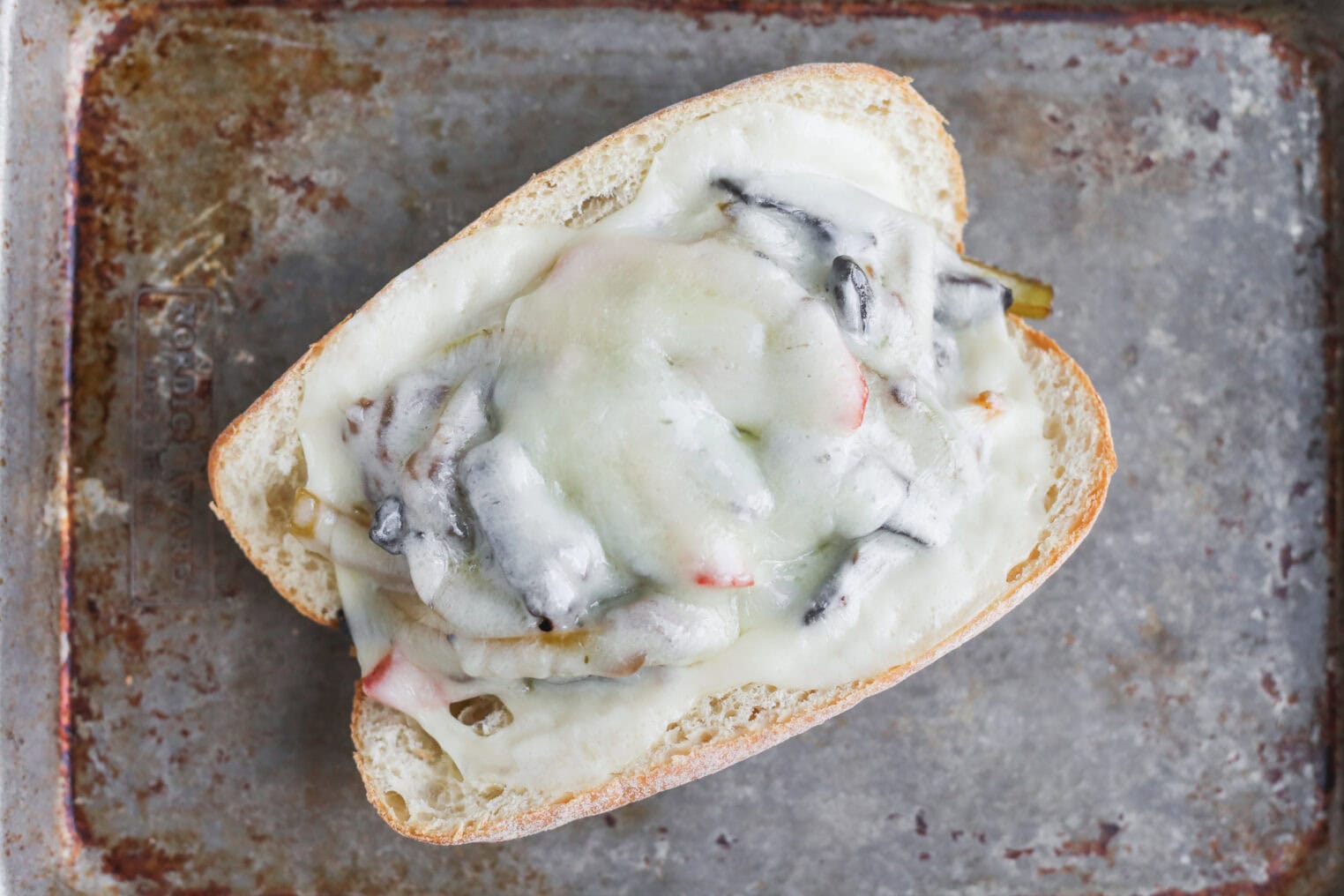 Portobello Cheesesteak Sandwiches 7 A Toasted Portobello Cheesesteak Sandwich Roll Topped With Melted Cheese And Sautéed Vegetables, Including Mushrooms And Peppers, On A Rustic Metal Baking Sheet.