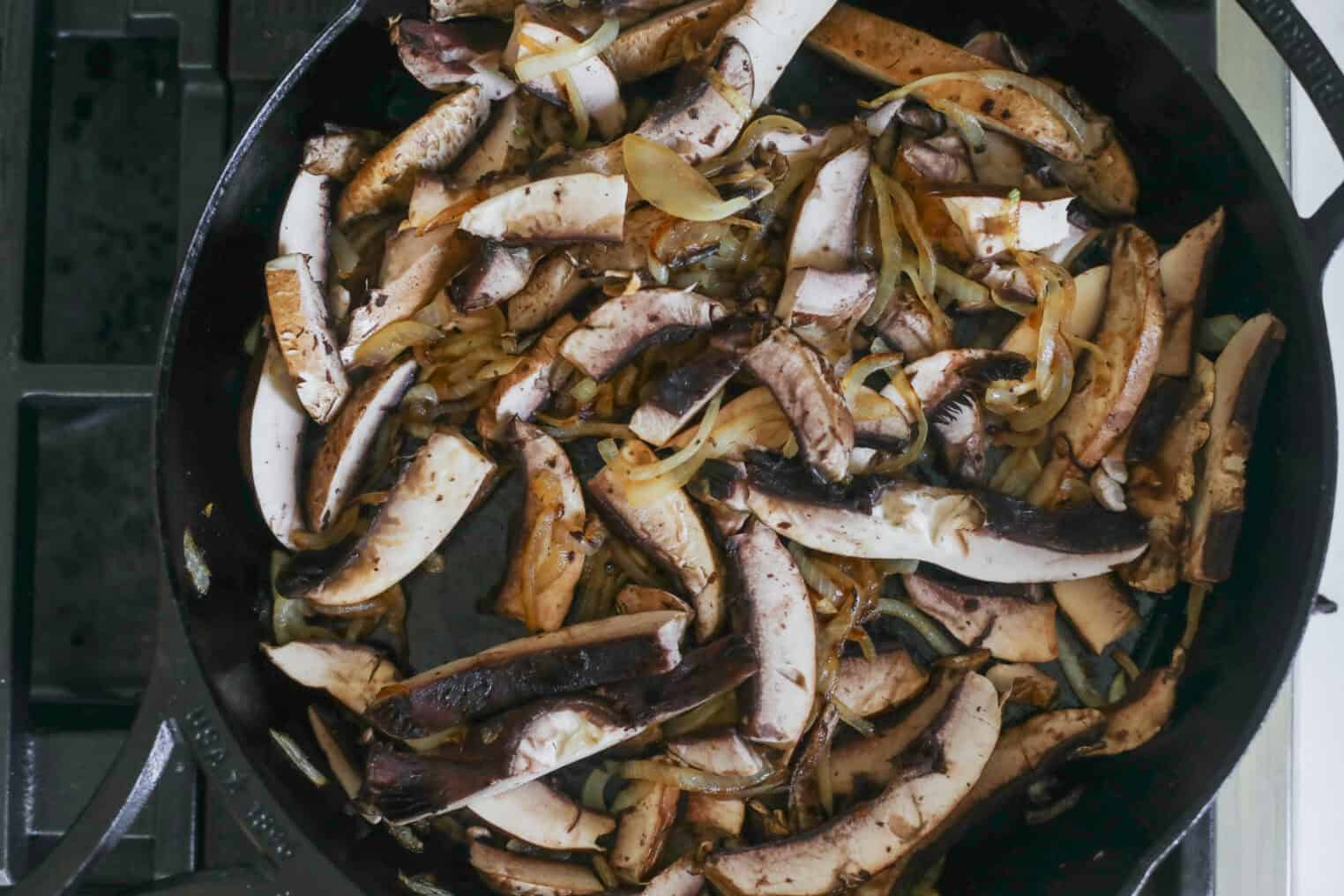Portobello Cheesesteak Sandwiches 4 A Cast Iron Skillet On A Stove Filled With Sautéed Sliced Mushrooms And Onions, Cooked Until Browned—The Perfect Base For Savory Portobello Cheesesteak Sandwiches.