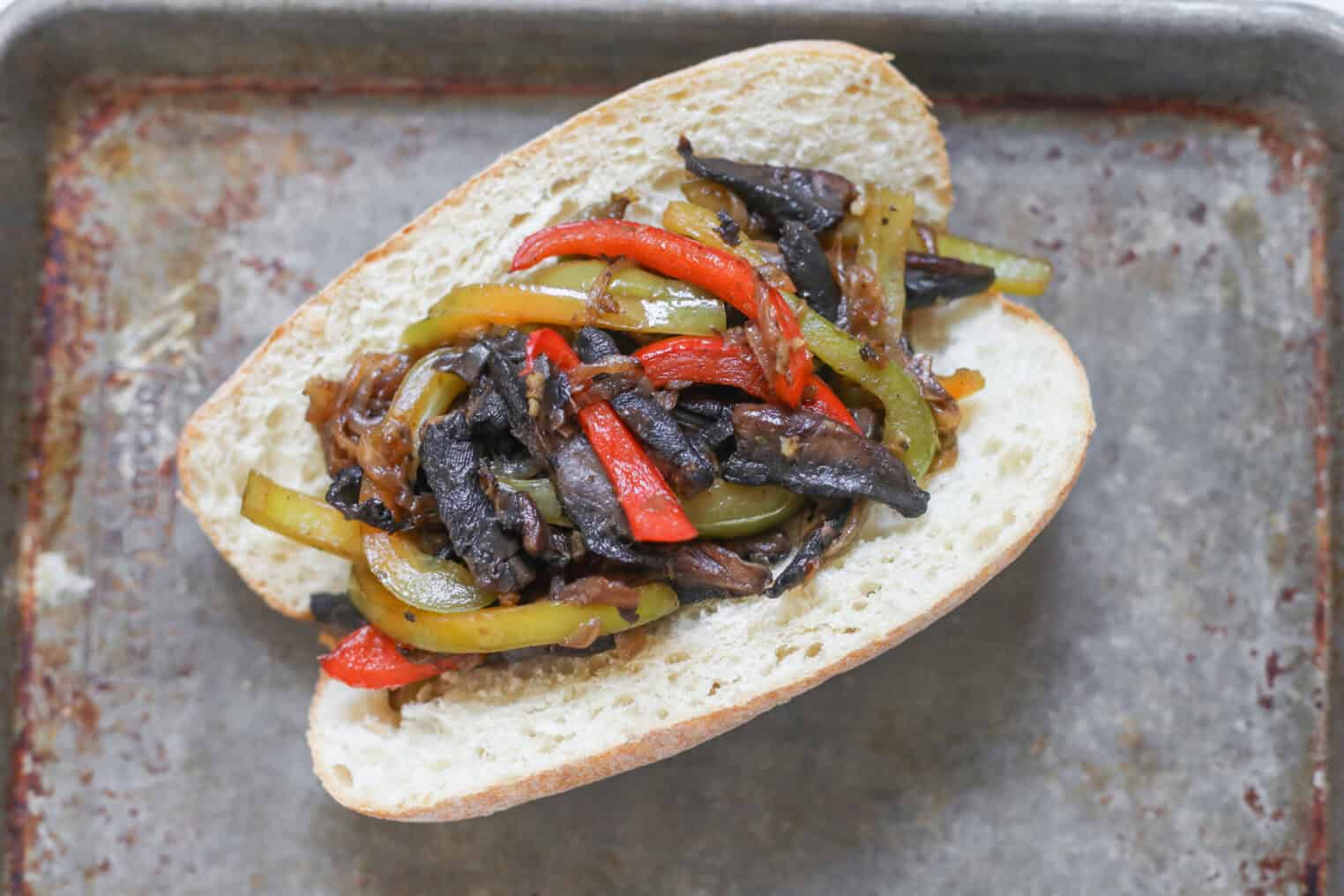 Portobello Cheesesteak Sandwiches 6 A Portobello Cheesesteak Sandwich On A Metal Tray, Filled With Sautéed Mushrooms, Red And Green Bell Peppers, And Caramelized Onions.