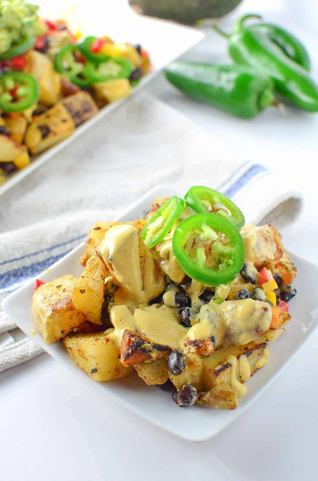 Vegan Potato Nachos! Crispy potatoes piled high with dairy-free cheese sauce, peppers, black beans, and guac! Gluten-Free and Vegan | www.delishknowledge.com