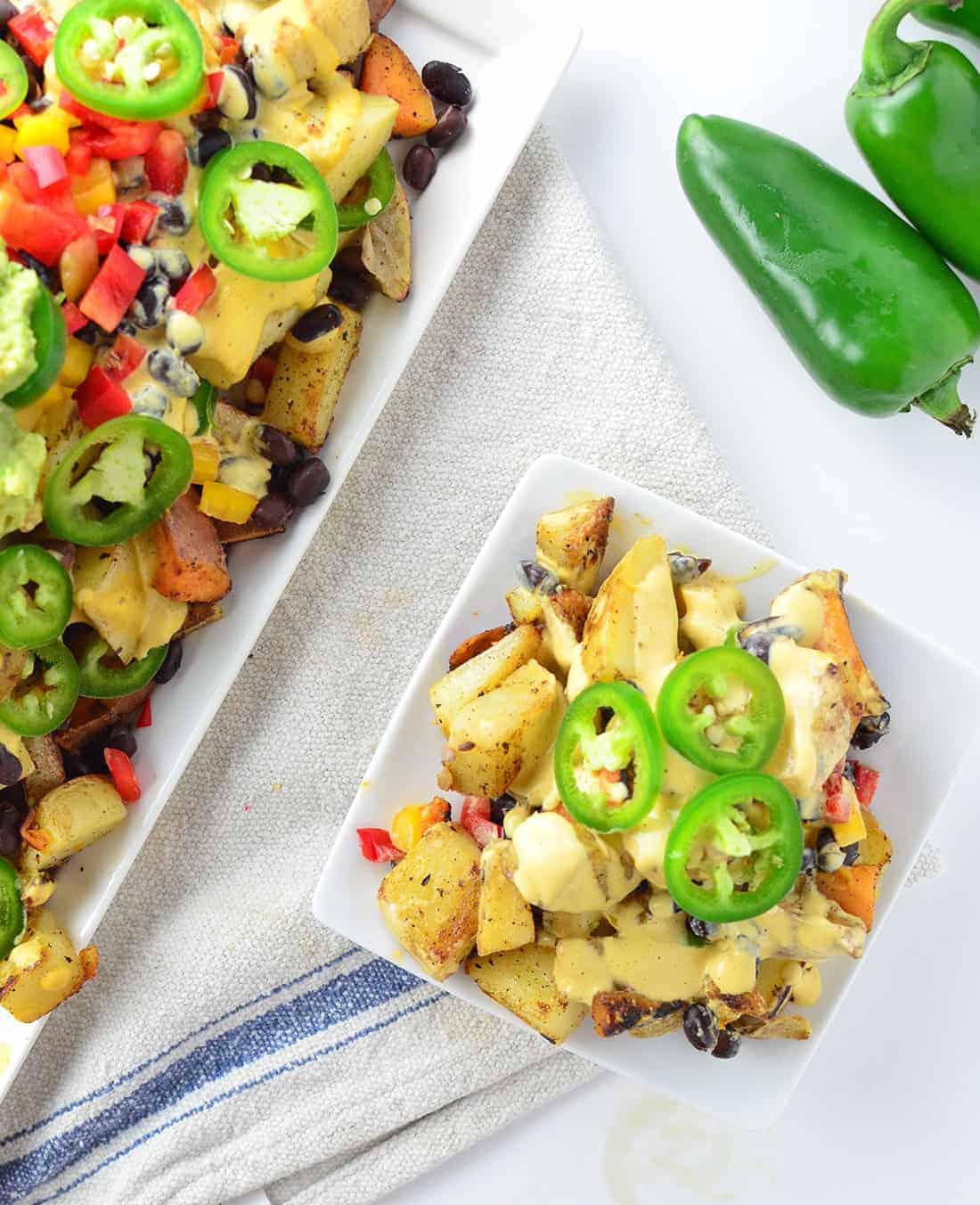 Vegan Potato Nachos! Crispy potatoes piled high with dairy-free cheese sauce, peppers, black beans, and guac! Gluten-Free and Vegan | www.delishknowledge.com