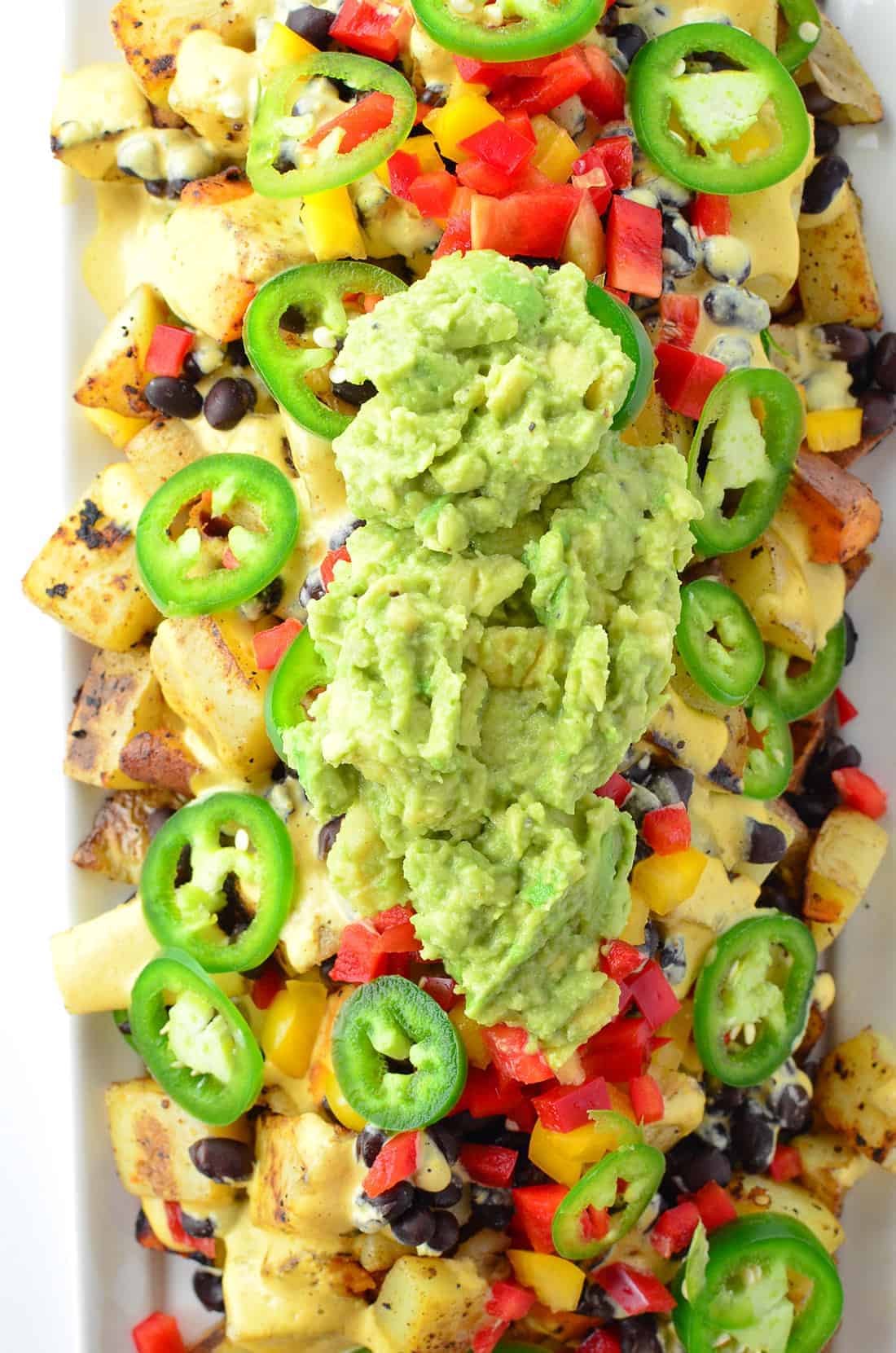 Vegan Potato Nachos! Crispy potatoes piled high with dairy-free cheese sauce, peppers, black beans, and guac! Gluten-Free and Vegan | www.delishknowledge.com