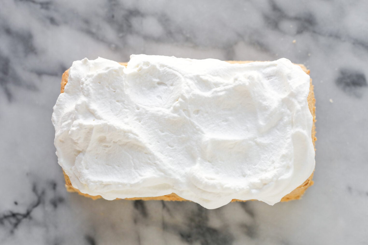 A Rectangular Pumpkin Icebox Cake Topped With A Thick, Uneven Layer Of Whipped Cream Sits On A Gray Marble Surface.