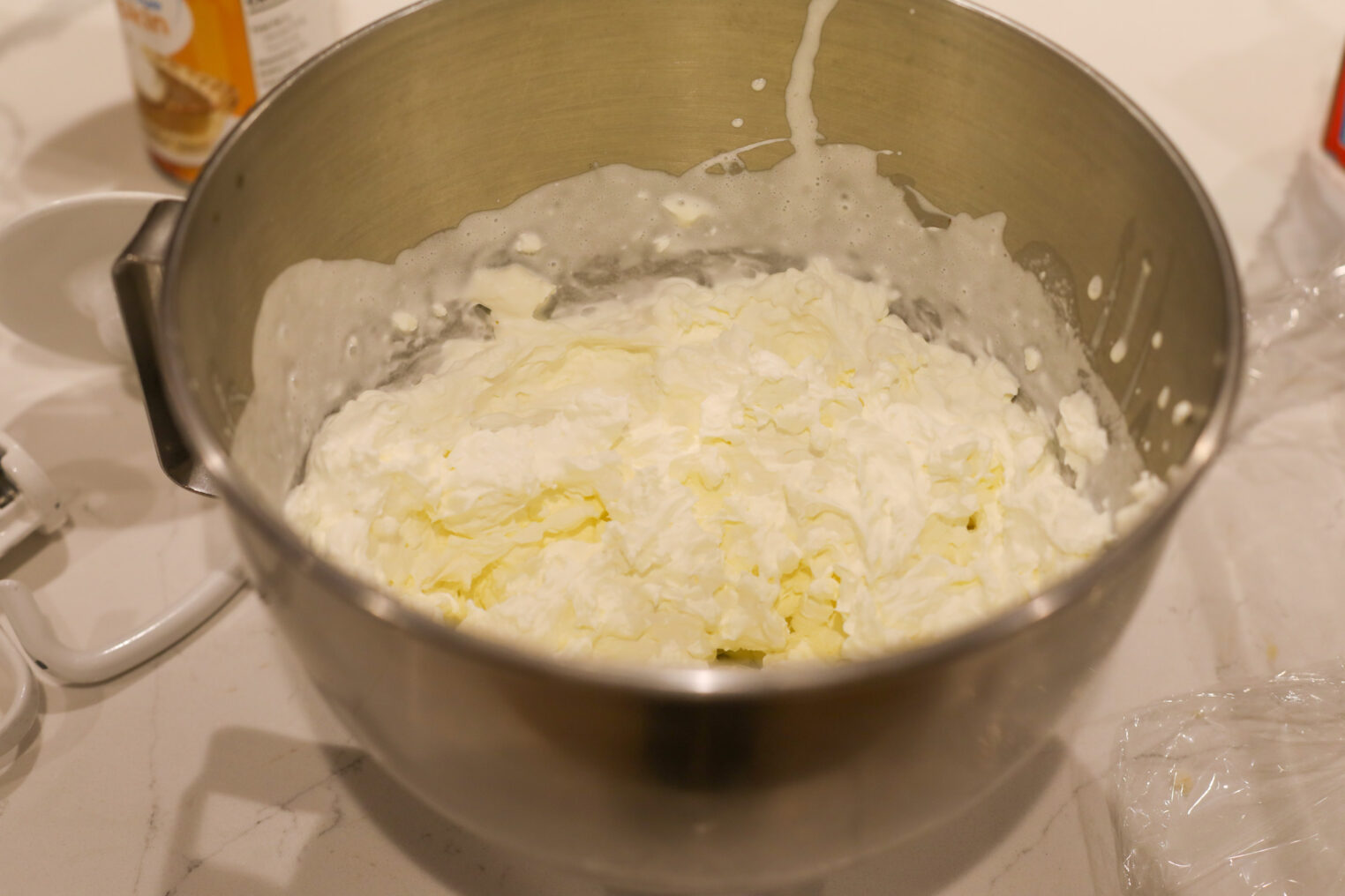 A Metal Mixing Bowl Filled With Whipped Cream Or Partly Whipped Butter, Sitting On A Kitchen Counter—Perfect For Making Pumpkin Icebox Cake. Some Cream Splatters Are Visible On The Sides Of The Bowl.