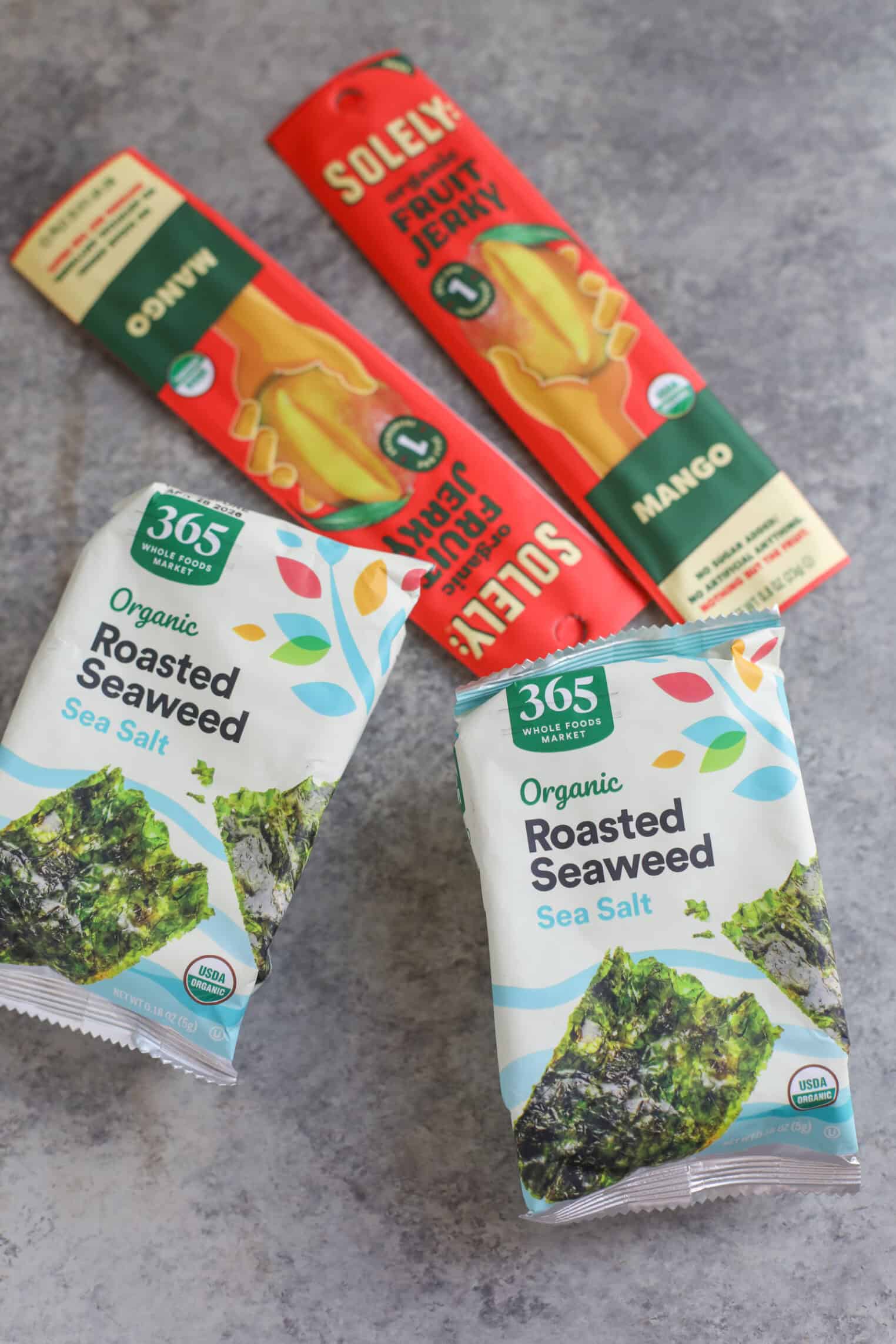 Registered Dietitian Approved Road Trip Summer Snacks 2 Perfect For Summer Road Trip Snacks, This Set Includes Two Packs Of 365 Organic Roasted Seaweed And Two Solely Mango Fruit Jerky Bars On A Gray Surface. The Seaweed Is In Green And White Packages, And The Mango Jerky Is Red And Yellow.