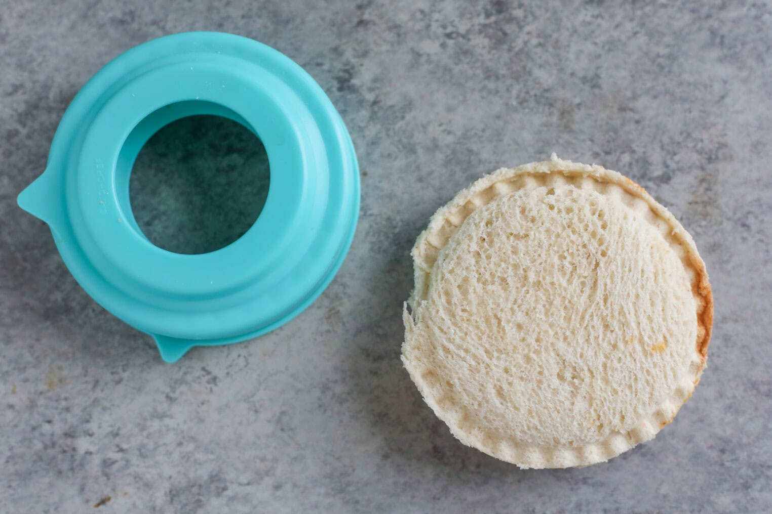 Registered Dietitian Approved Road Trip Summer Snacks 4 A Round Sandwich With Sealed Edges, Perfect For Summer Road Trip Snacks, Sits Next To A Blue Sandwich Cutter On A Gray Surface.