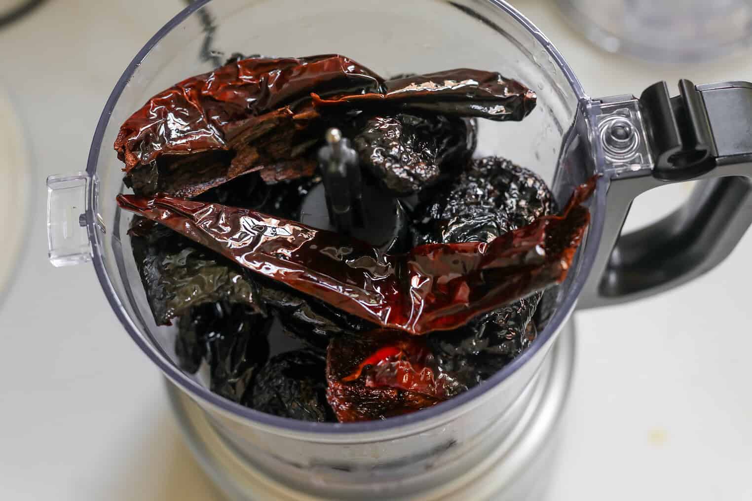 Dried Red And Dark Chilies In A Food Processor Bowl, Ready To Be Blended Into Salsa Macha, Viewed From Above On A Light Kitchen Surface.