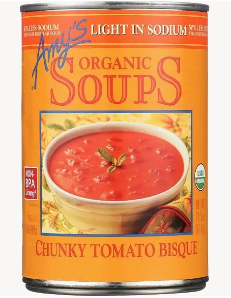 The 10 Healthiest Canned Soups 9 A Can Of Amy’s Organic Soups, Chunky Tomato Bisque Flavor, Labeled “Light In Sodium.” This Usda Organic Option Is Among The Healthiest Canned Soups, Shown With A Bowl Of Tomato Soup And Fresh Herbs.