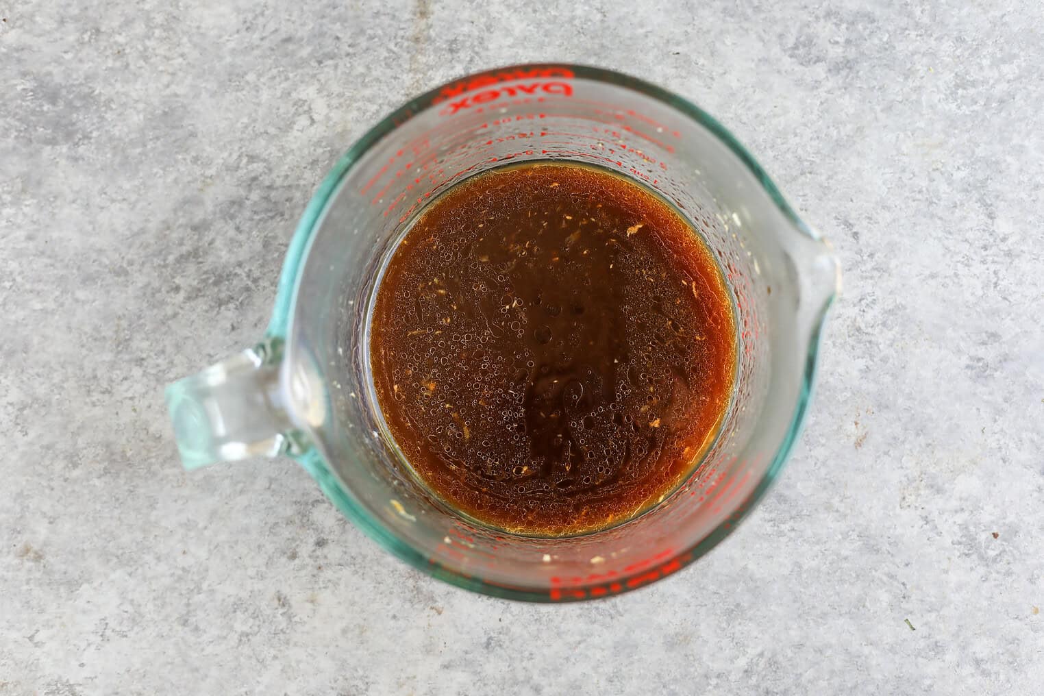 Sesame Garlic Stir Fry Noodles 4 A Glass Measuring Cup Filled With A Brown Liquid Mixture, Likely A Marinade Or Sauce For Stir Fry Noodles, Sits On A Gray Textured Surface.