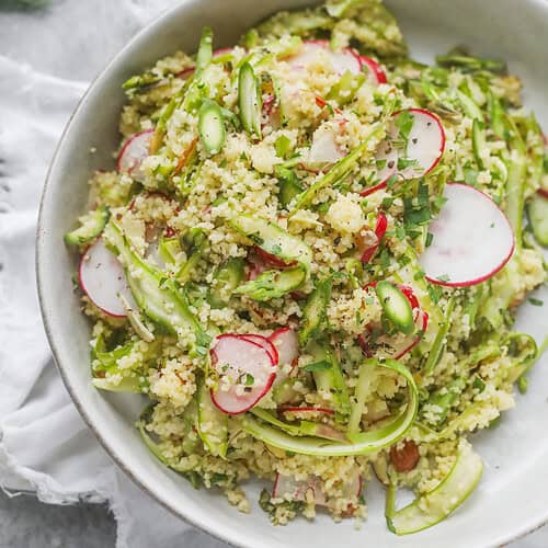 Shaved Asparagus Spring Salad 11 A Bowl Of Couscous Features A Vibrant Shaved Asparagus Spring Salad, With Thinly Sliced Radishes And Fresh Herbs, Served On A Light Gray Surface With A White Cloth Underneath.