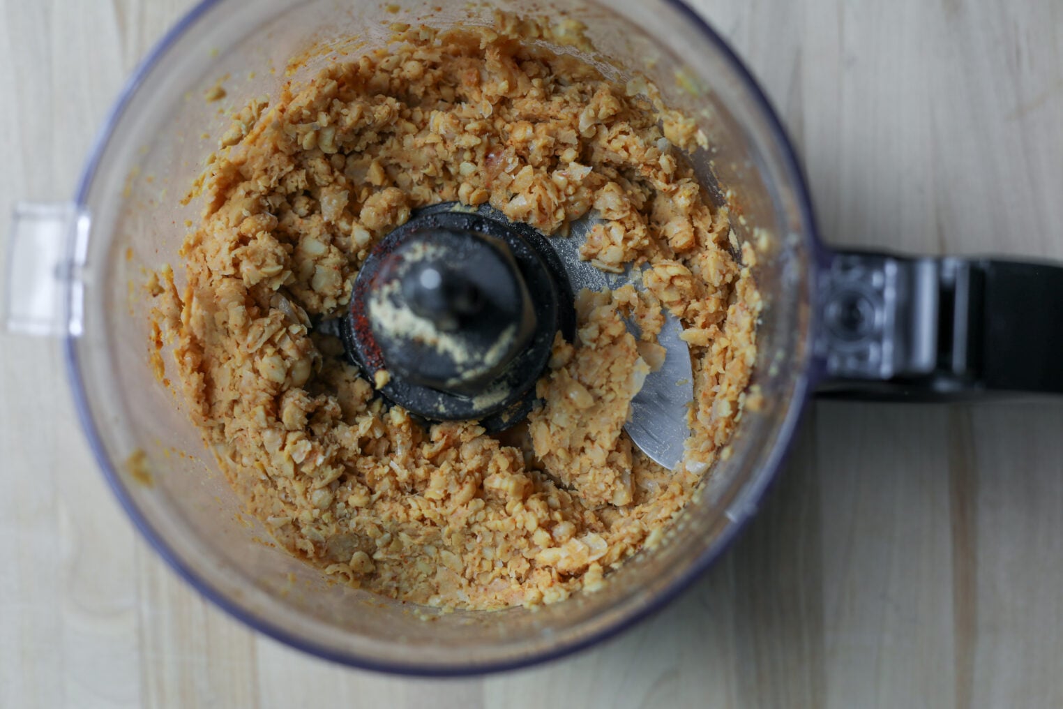 Smashed Chickpea Tacos 3 A Food Processor Bowl Filled With A Chunky, Beige-Orange Mixture—Possibly Ground Chickpeas Or Beans For Smashed Chickpea Tacos—Sits On A Light Wooden Surface.